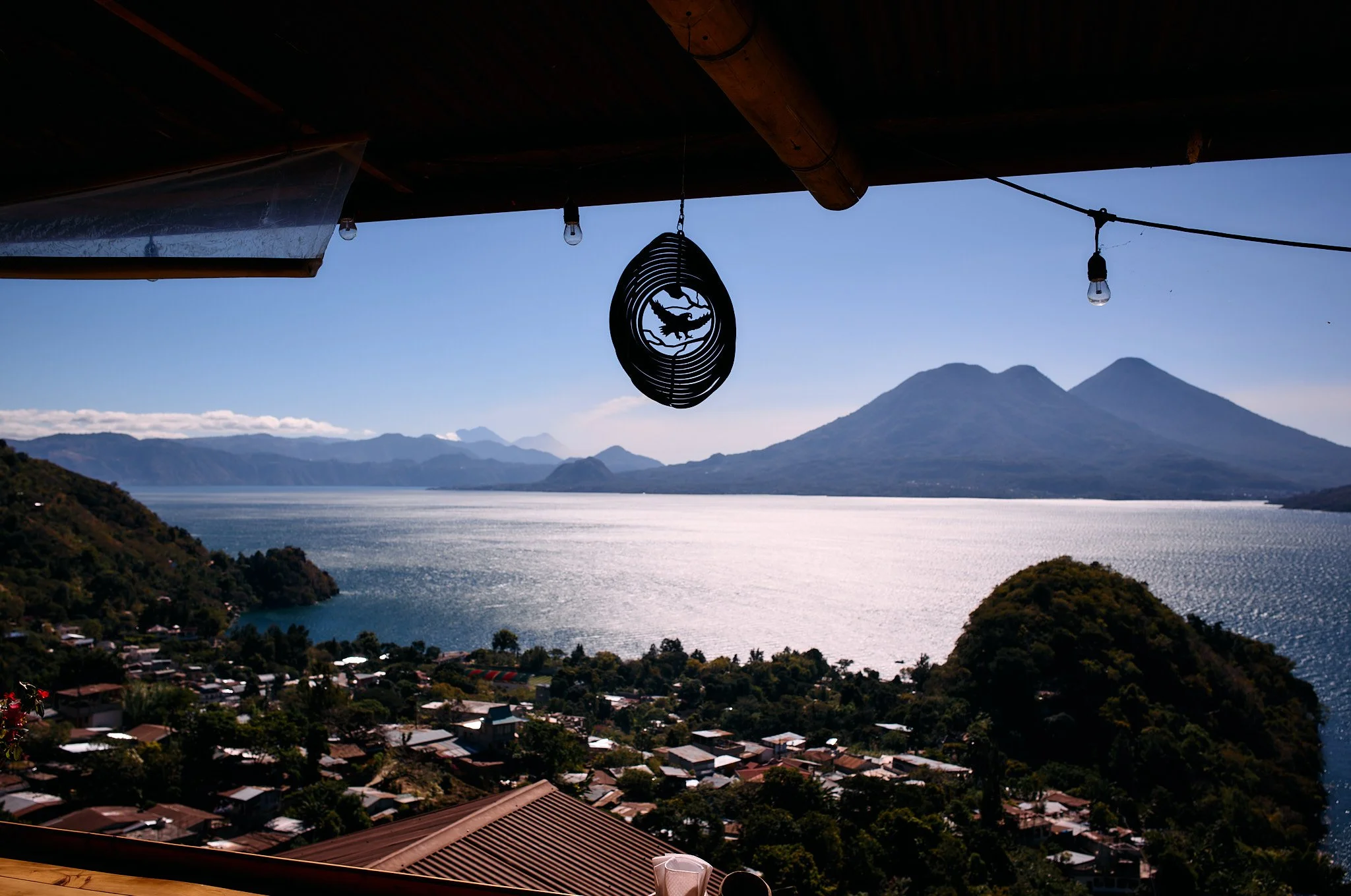 A scenic view of a lake with mountains in the background, seen from a balcony with hanging lights and a wind chime.