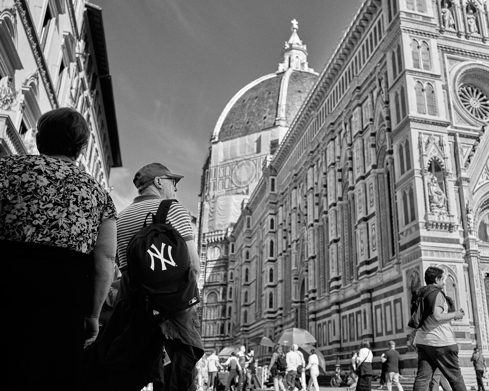 People walking in front of the Florence Cathedral, also known as the Cathedral of Santa Maria del Fiore, in Florence, Italy. The cathedral's large dome and ornate facade are visible.