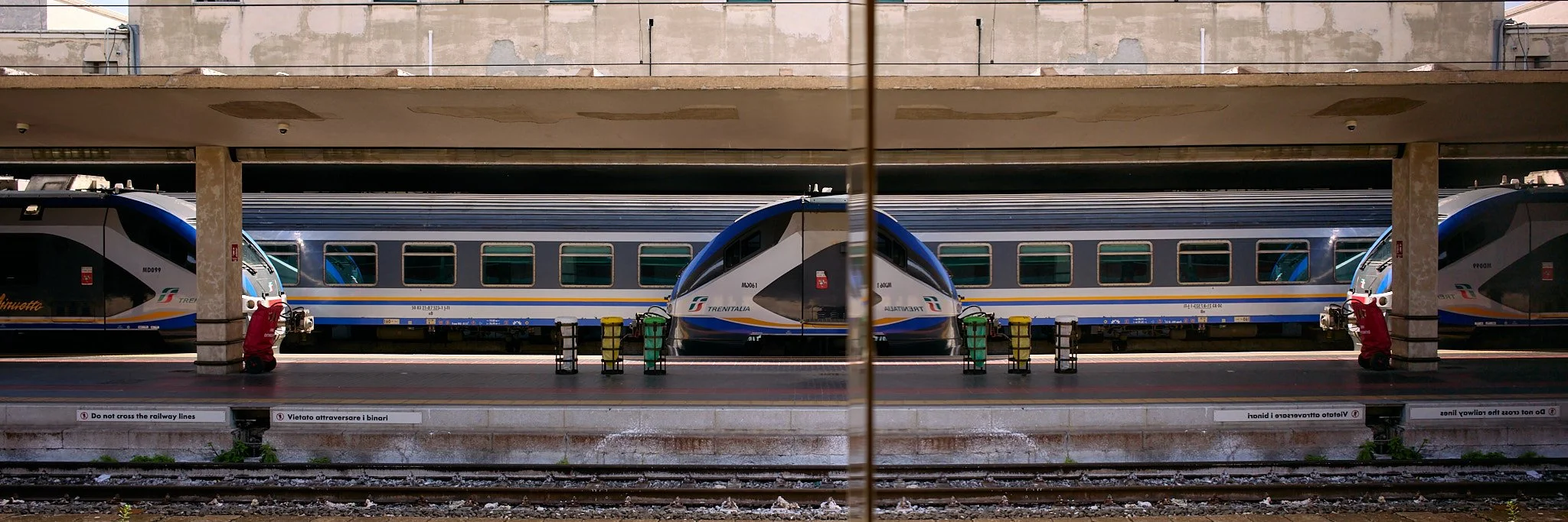 Front view of a modern high-speed train parked at a train station platform, with safety signs and barriers in the foreground.