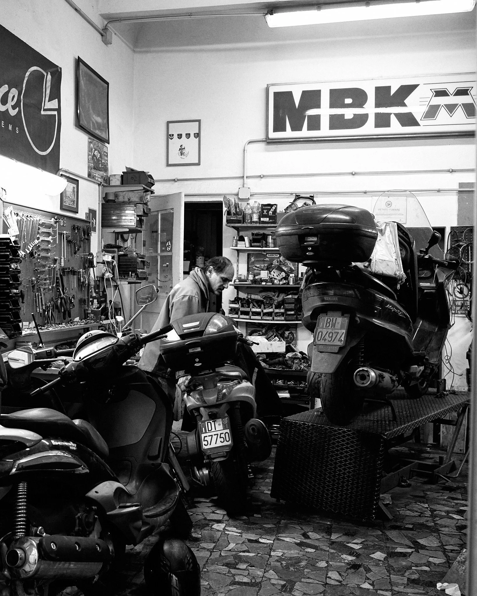 A man working in a motorcycle repair shop with several motorcycles and tools around him.