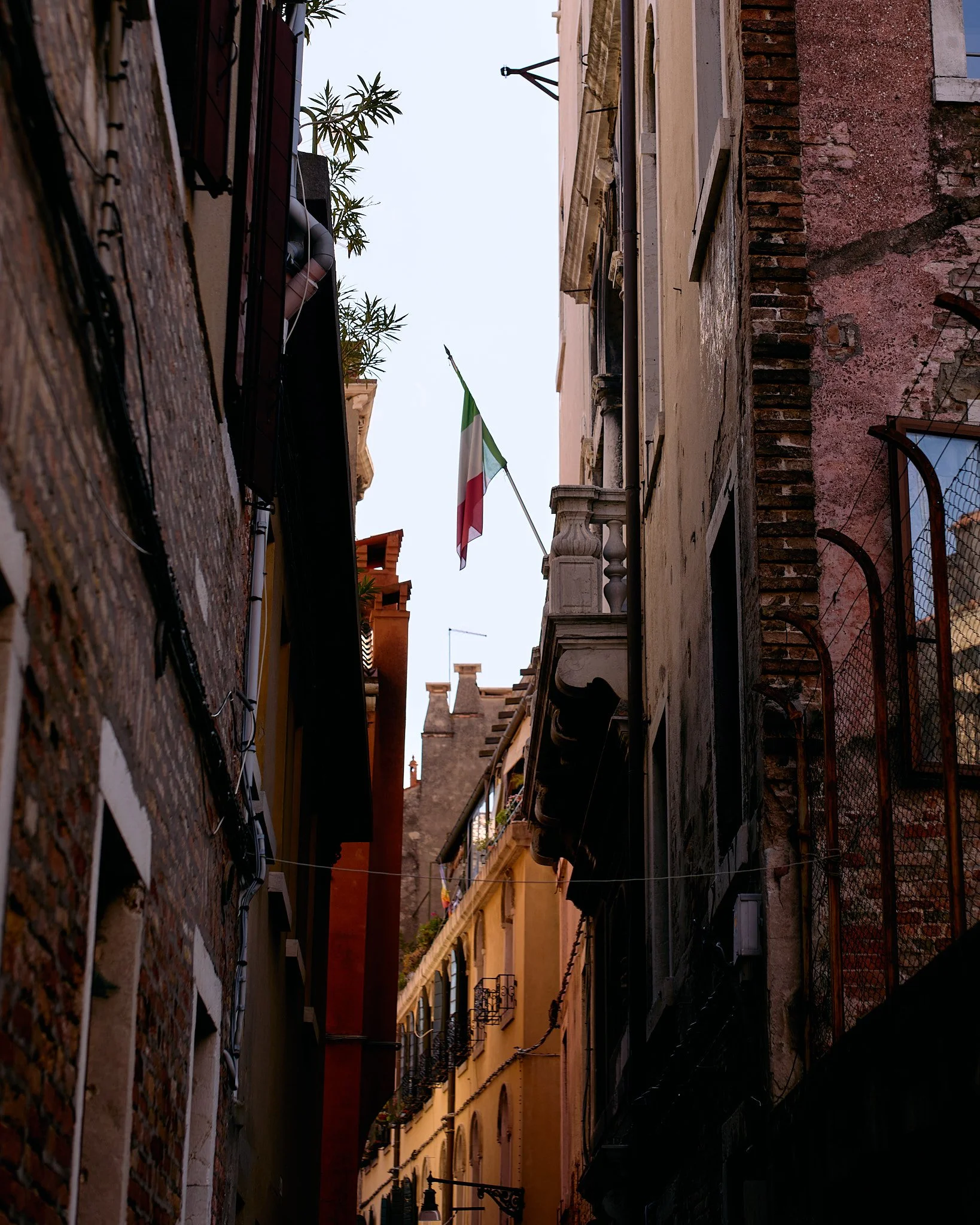 Narrow alleyway between old European buildings with an Italian flag flying above.