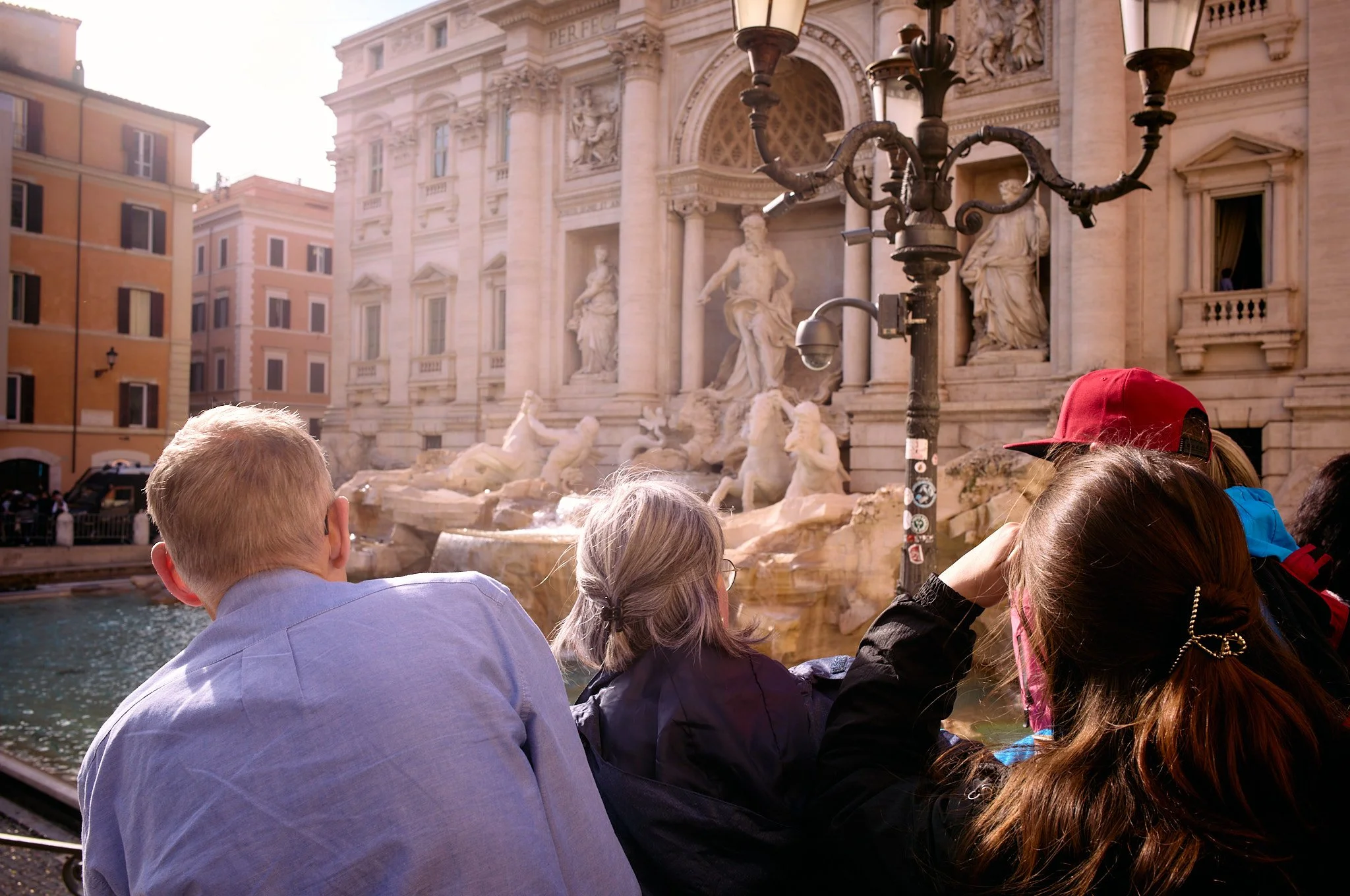 Tourists sitting by the Trevi Fountain in Rome, Italy, admiring the ornate baroque sculptures and water features