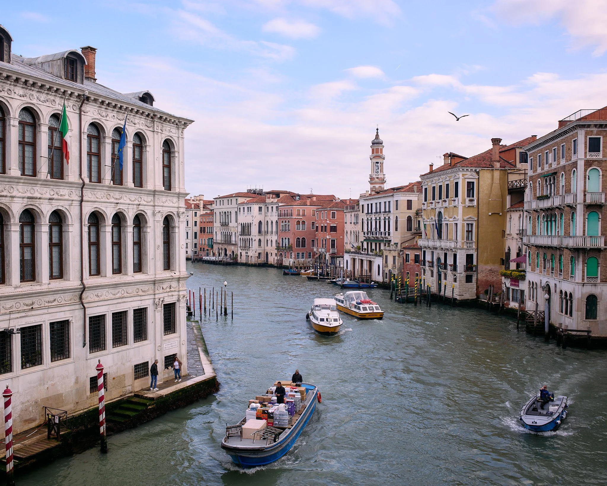 Venetian canal with boats and historic buildings along the waterway under a partly cloudy sky.