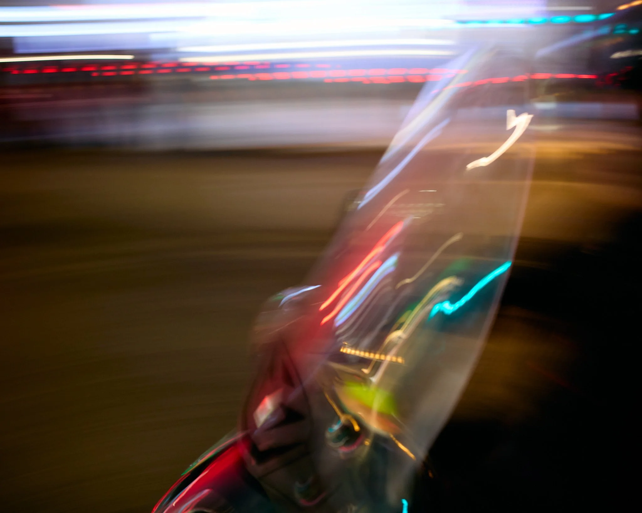 A blurry photo showing city lights and reflections at night, with streaks of colorful neon lights and motion blur.