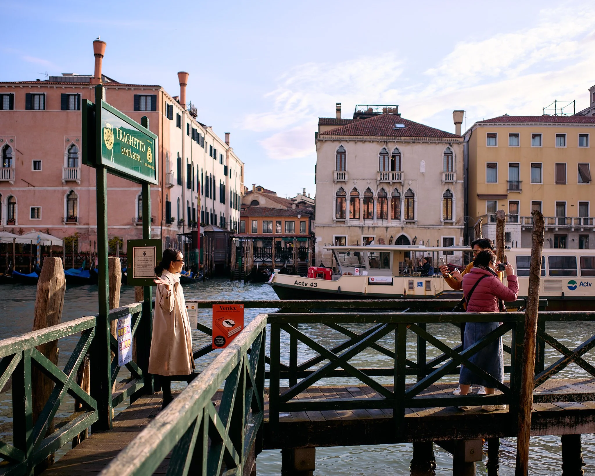 People at a Venice canal dock with boats and colorful buildings in the background.