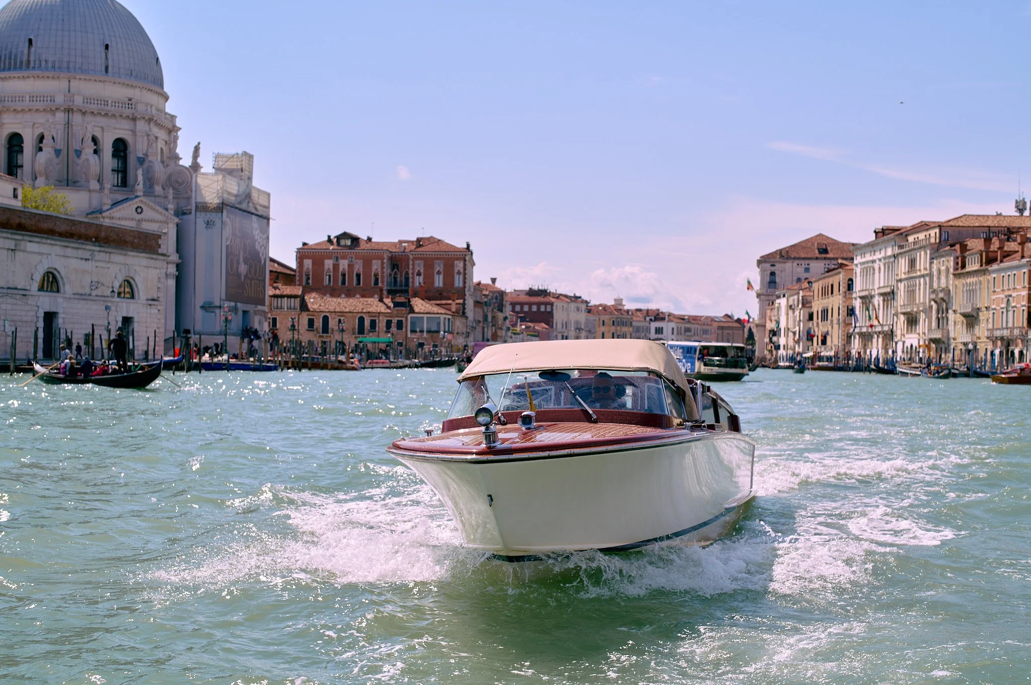A boat cruising through the canal in Venice, Italy, with historic buildings on either side and the sun shining on the water.