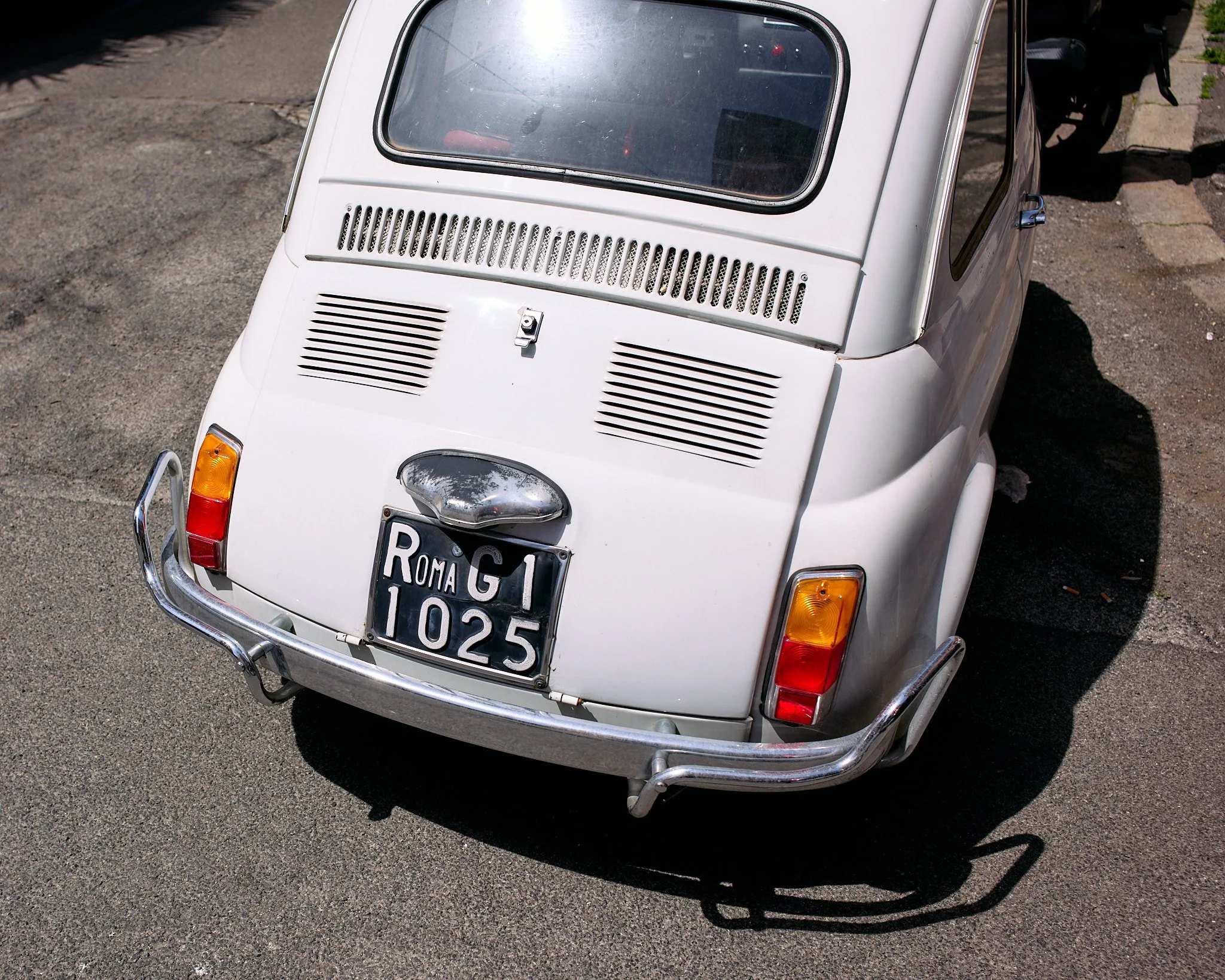 A white vintage Fiat 500 car parked on the street, showing the rear view with an Italian license plate and a chrome bumper.