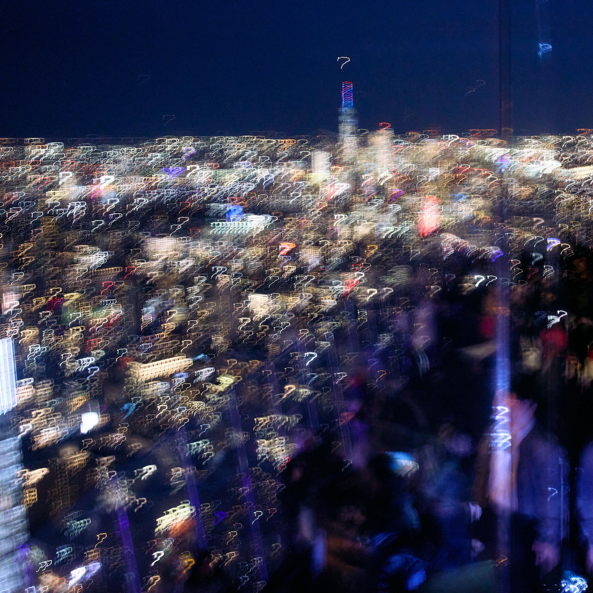 Nighttime cityscape with skyscrapers and a crowd of people, blurry due to camera shake or movement.