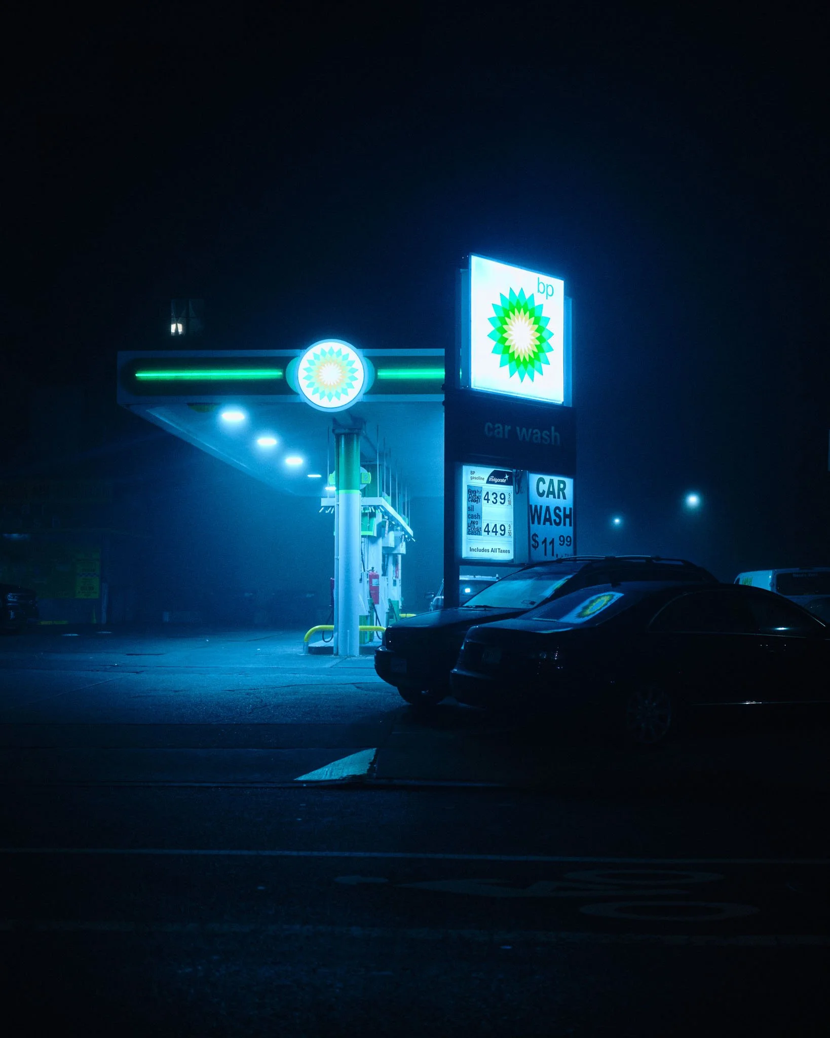 Nighttime scene of a BP gas station with illuminated signs and cars parked nearby.