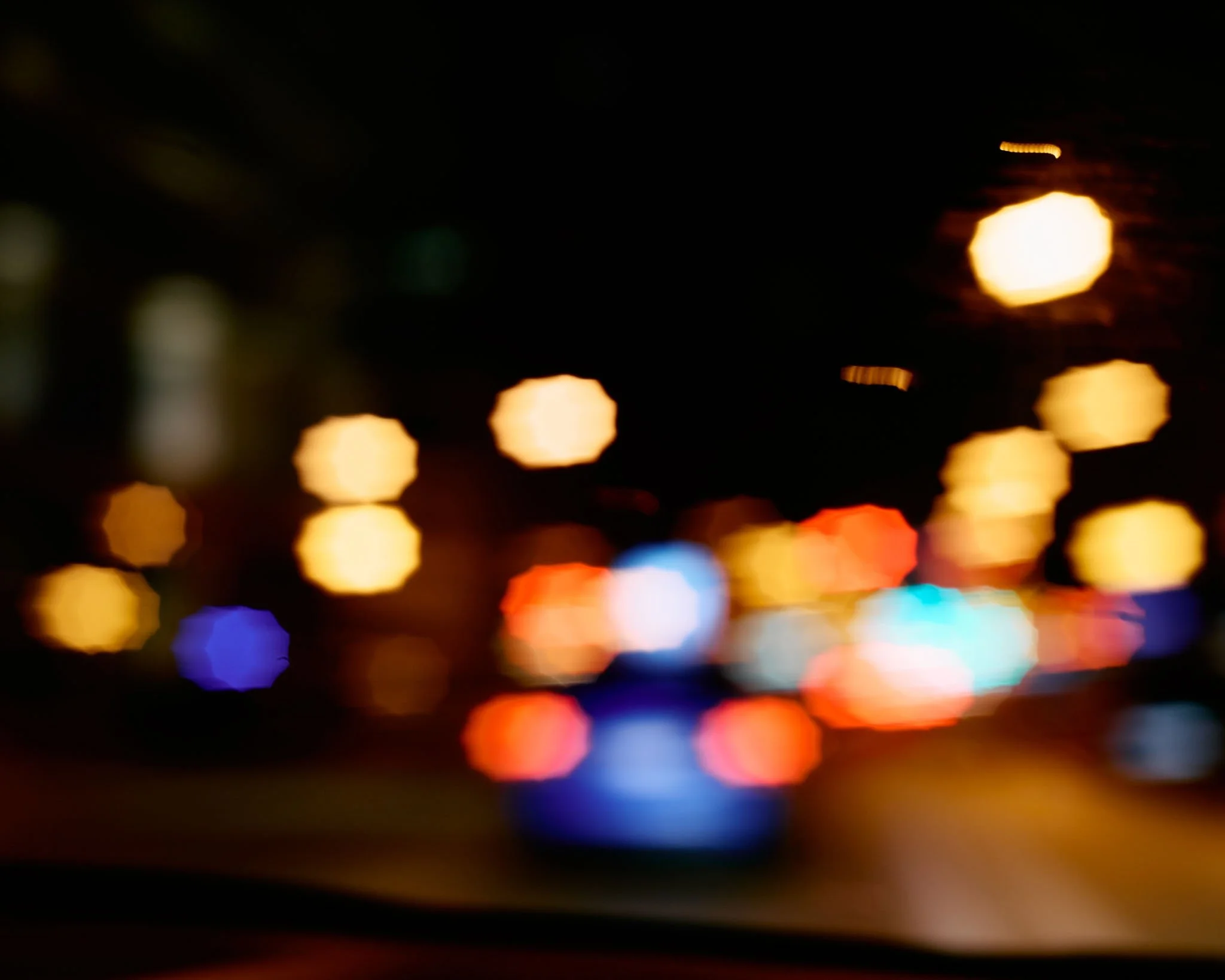Out of focus photograph of city street at night with bright blurred lights from vehicles and streetlights.