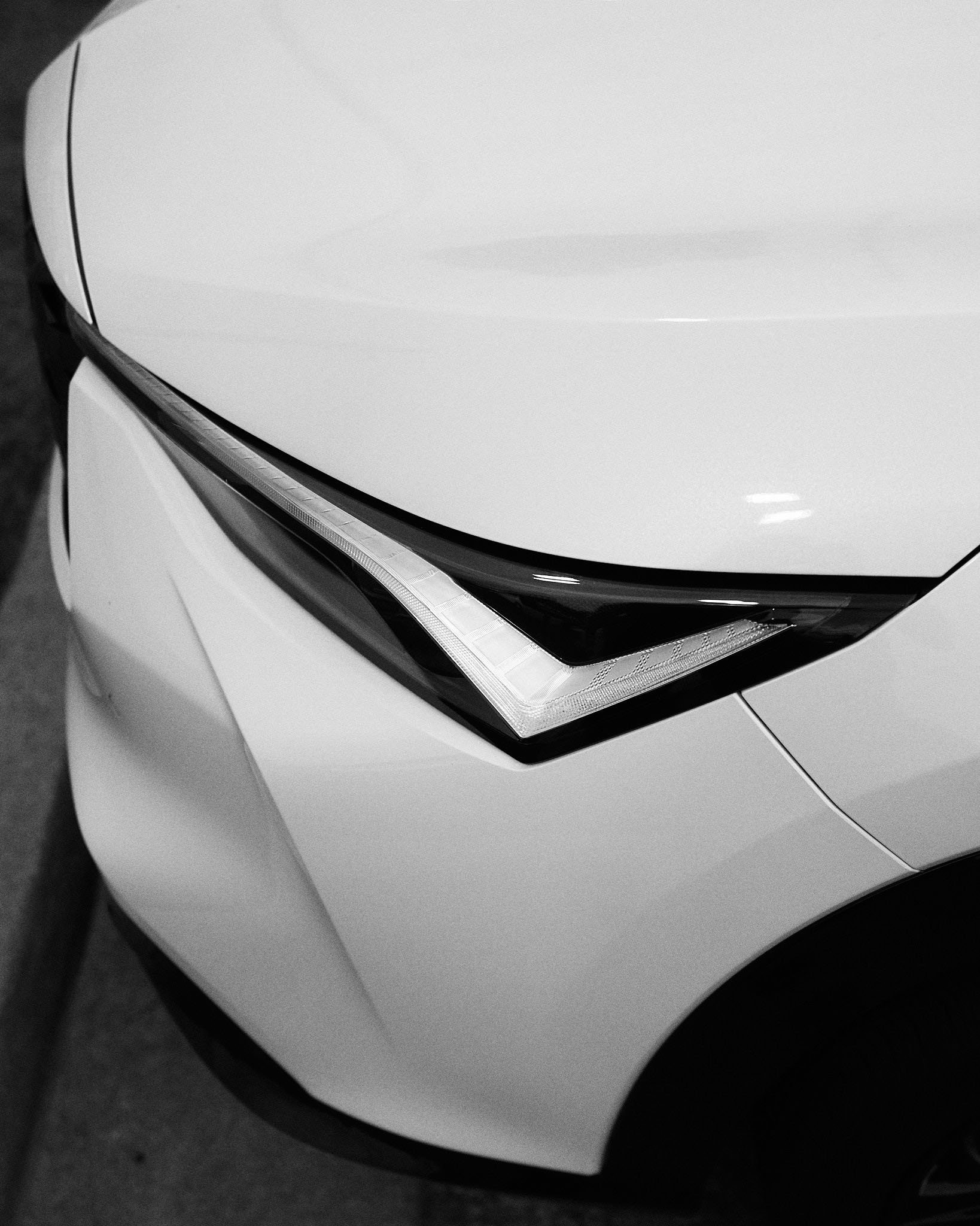 Close-up of a white car's front end, showcasing the headlight and part of the hood.