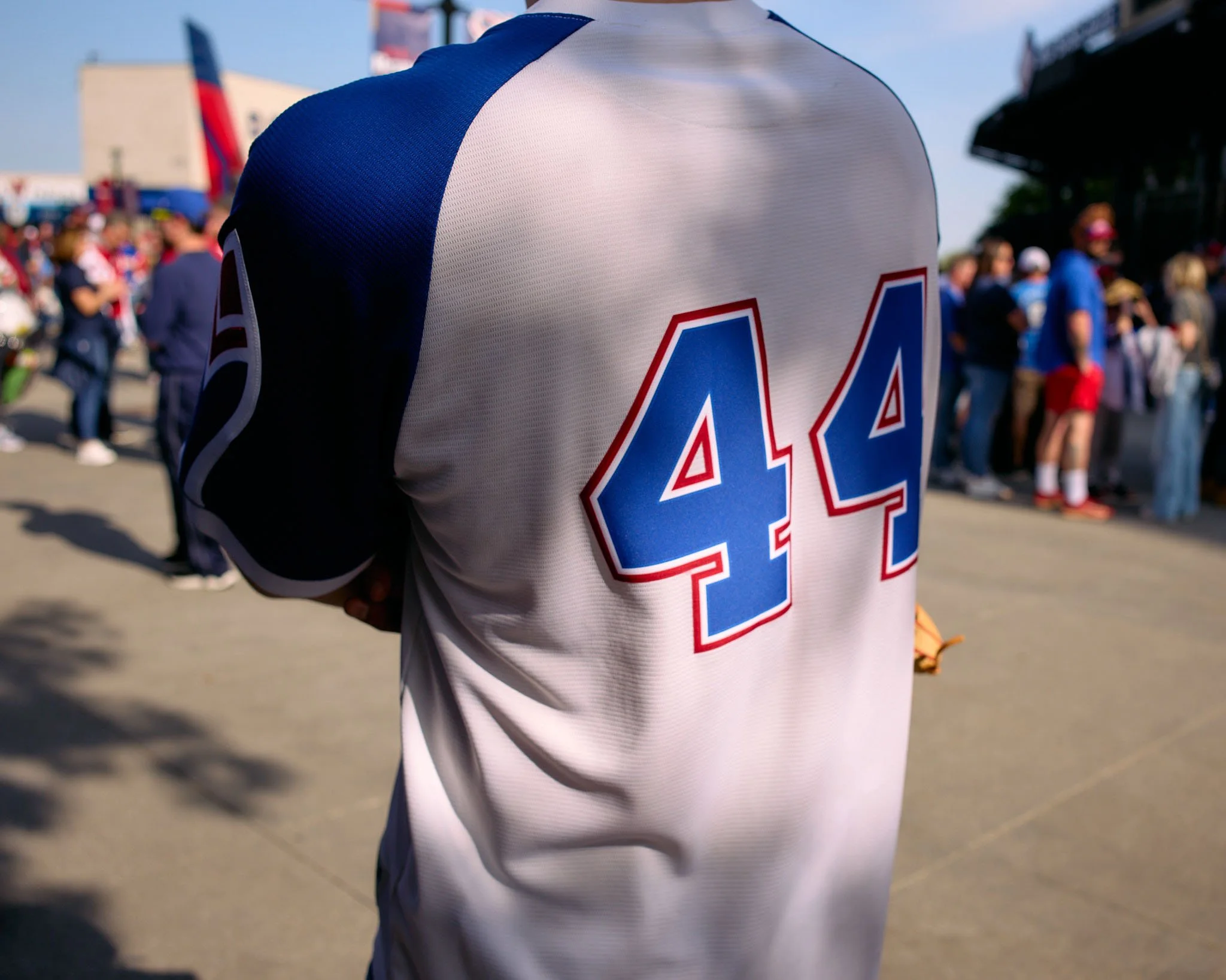 Back of a person wearing a white and blue sports jersey with the number 44 on it, in a crowd at an outdoor event.