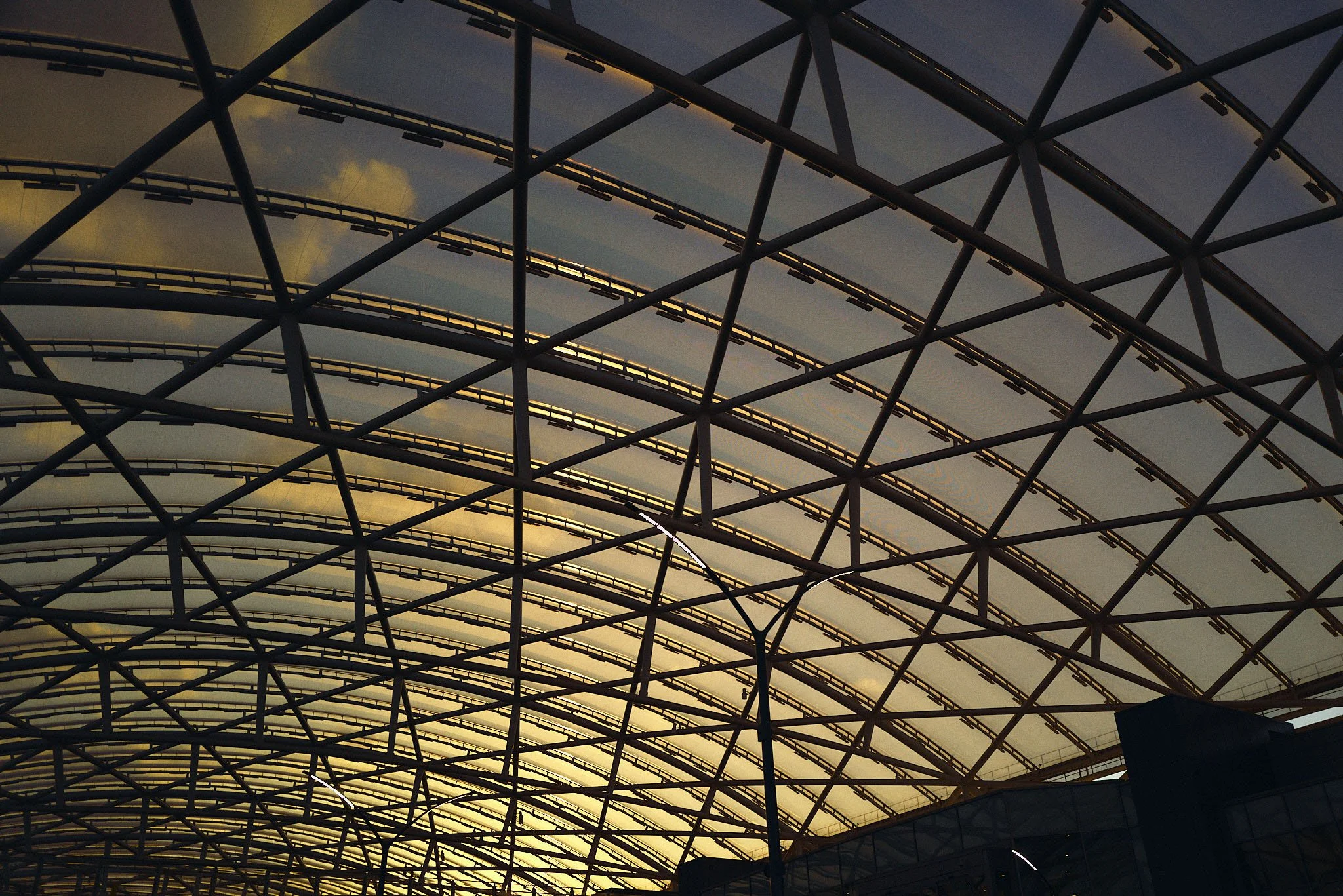 Interior of a large modern train station with a glass and metal arched ceiling structure at sunset.
