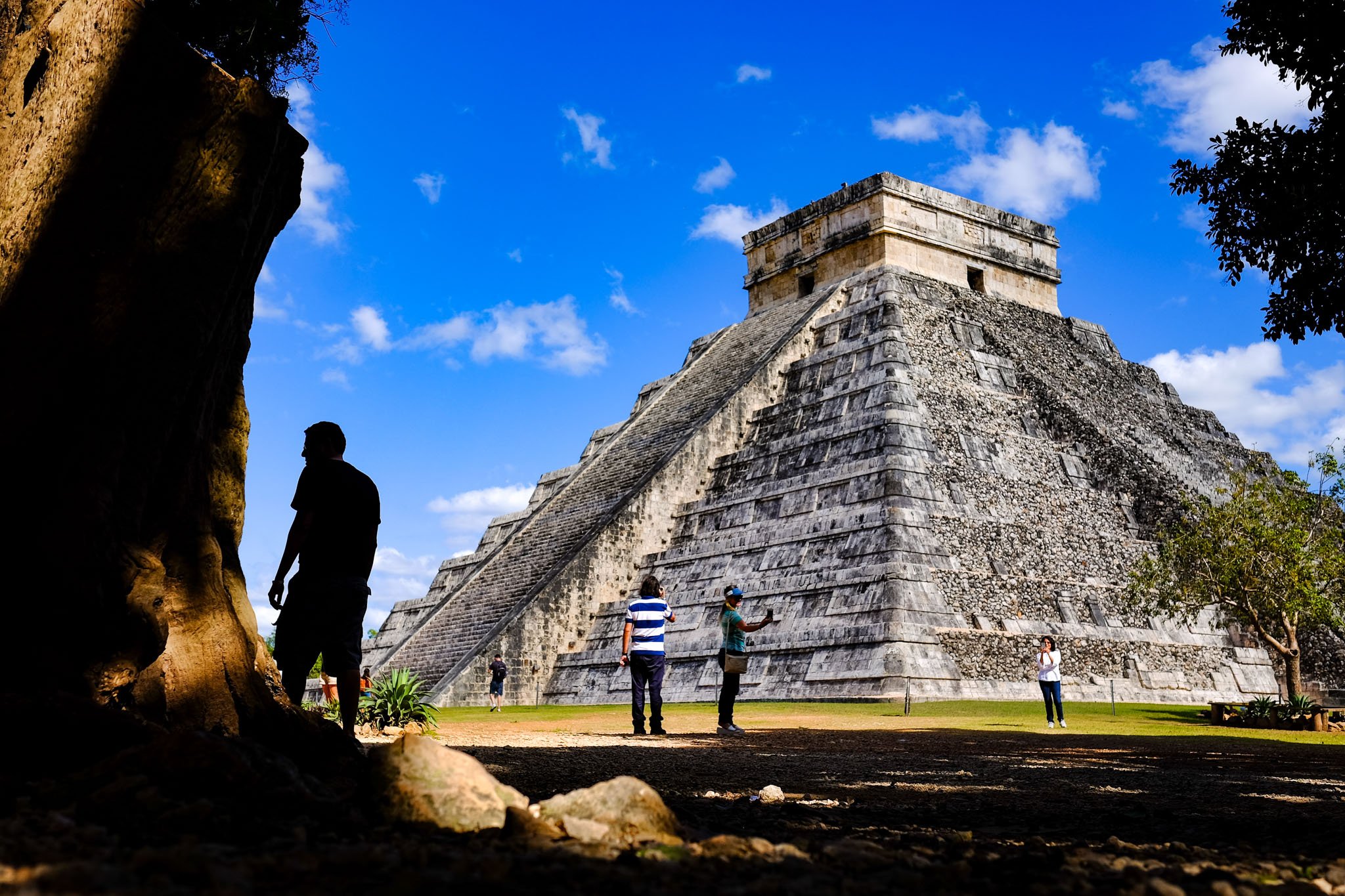 Mayan pyramid with tourists around it in a sunny sky.