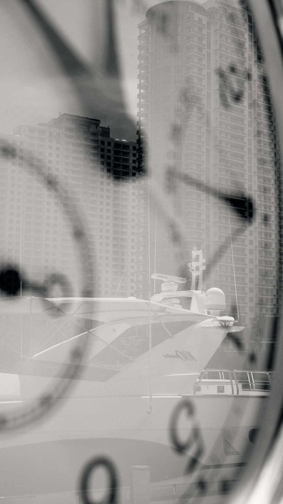 A boat docked near high-rise buildings, photograph taken through a window with raindrops or water spots on the glass in black and white.