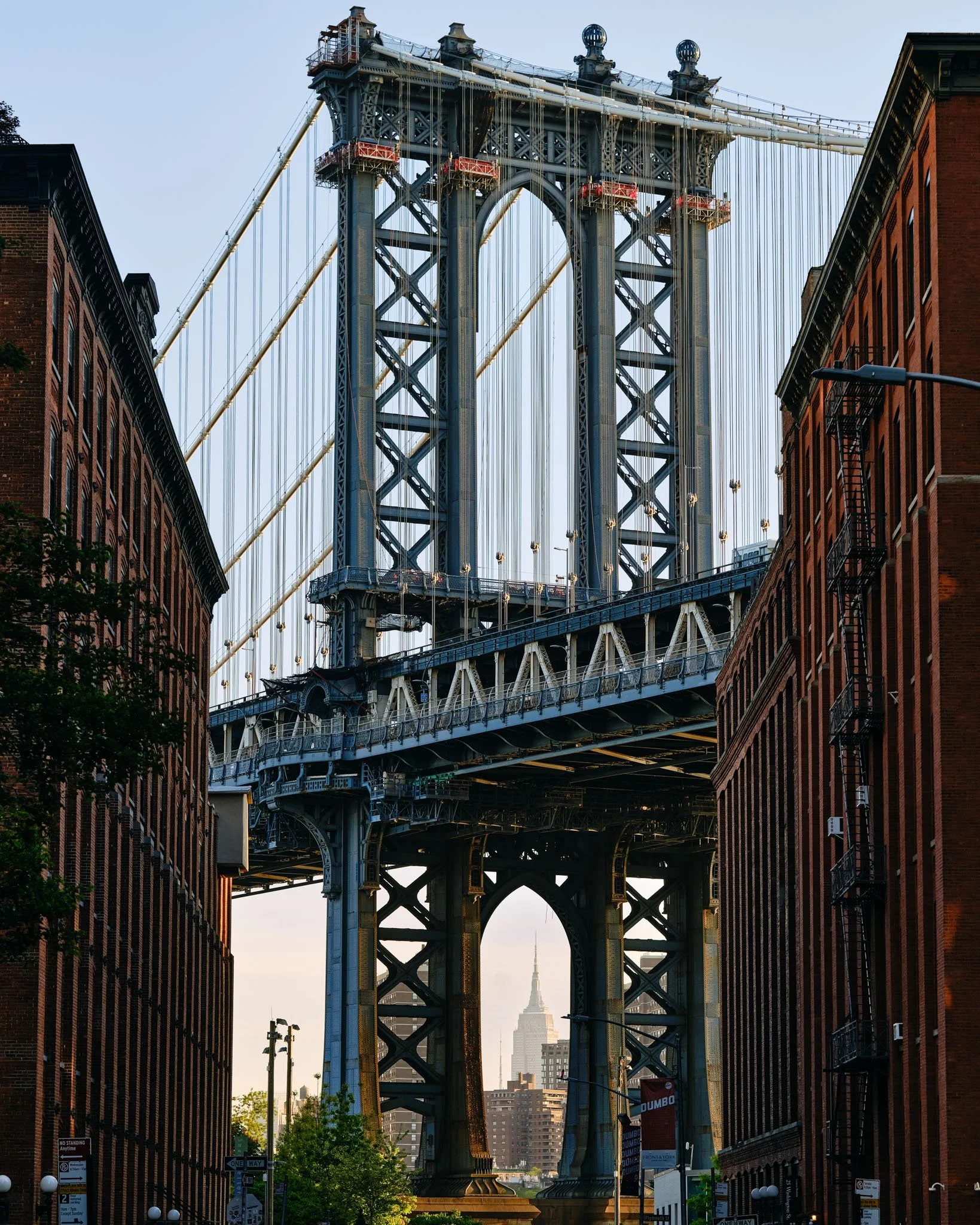 View of the Manhattan Bridge with the Empire State Building in the background, seen from a street between brick buildings.