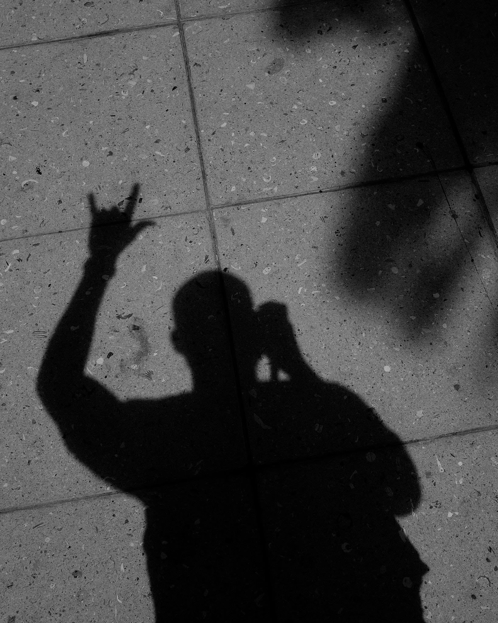Shadow of a person taking a photo on a tiled floor, making a peace sign with the hand.