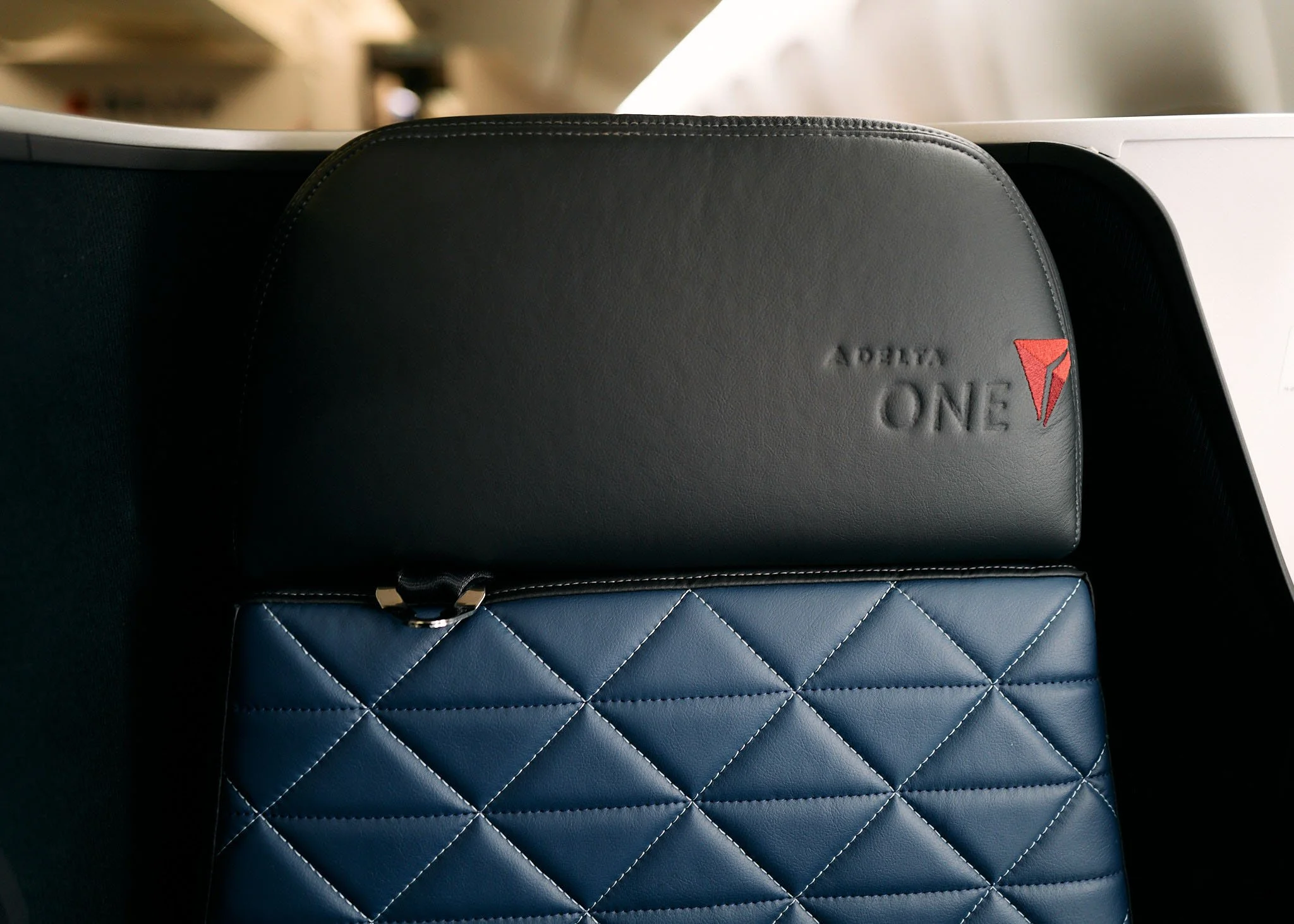 Two closed cases, one black with the word 'Delta One' embossed and a red Delta logo, stacked on top of a blue quilted case, on an aircraft seat tray table.