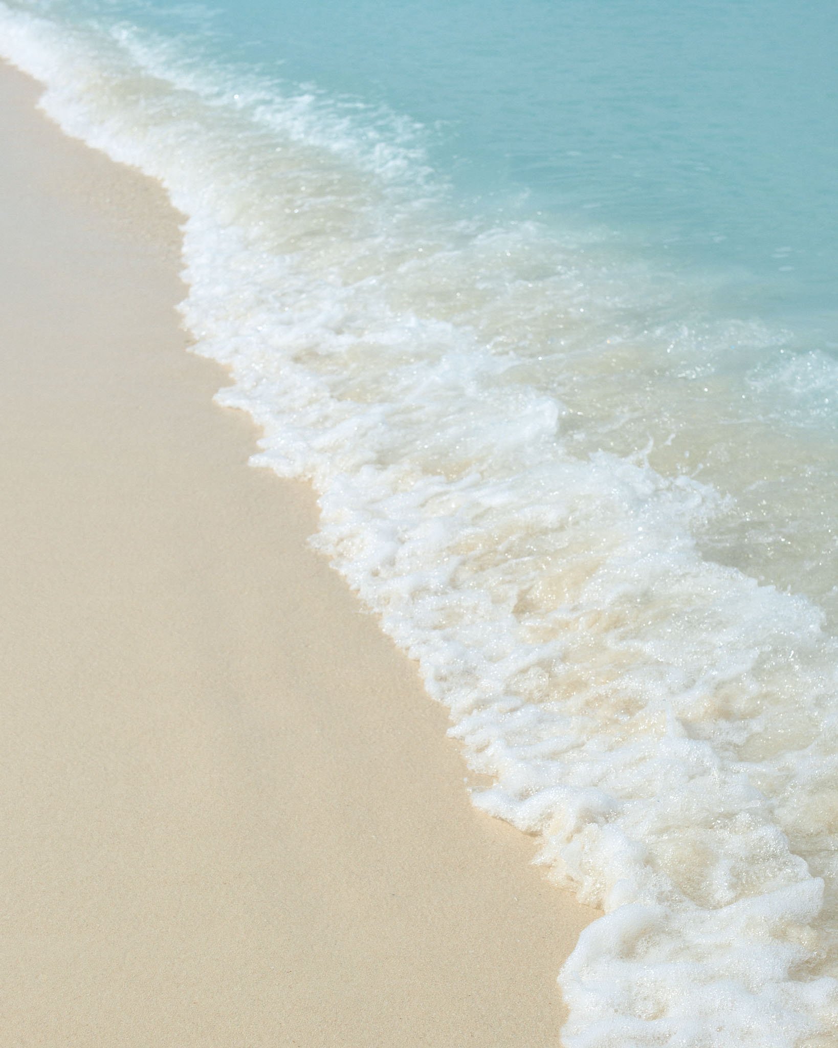 Calm ocean waves gently reaching sandy beach shore.