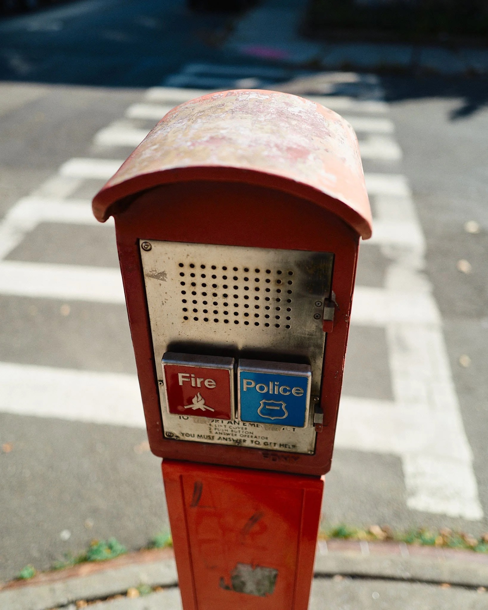 Red emergency call box with fire and police buttons, near a crosswalk.