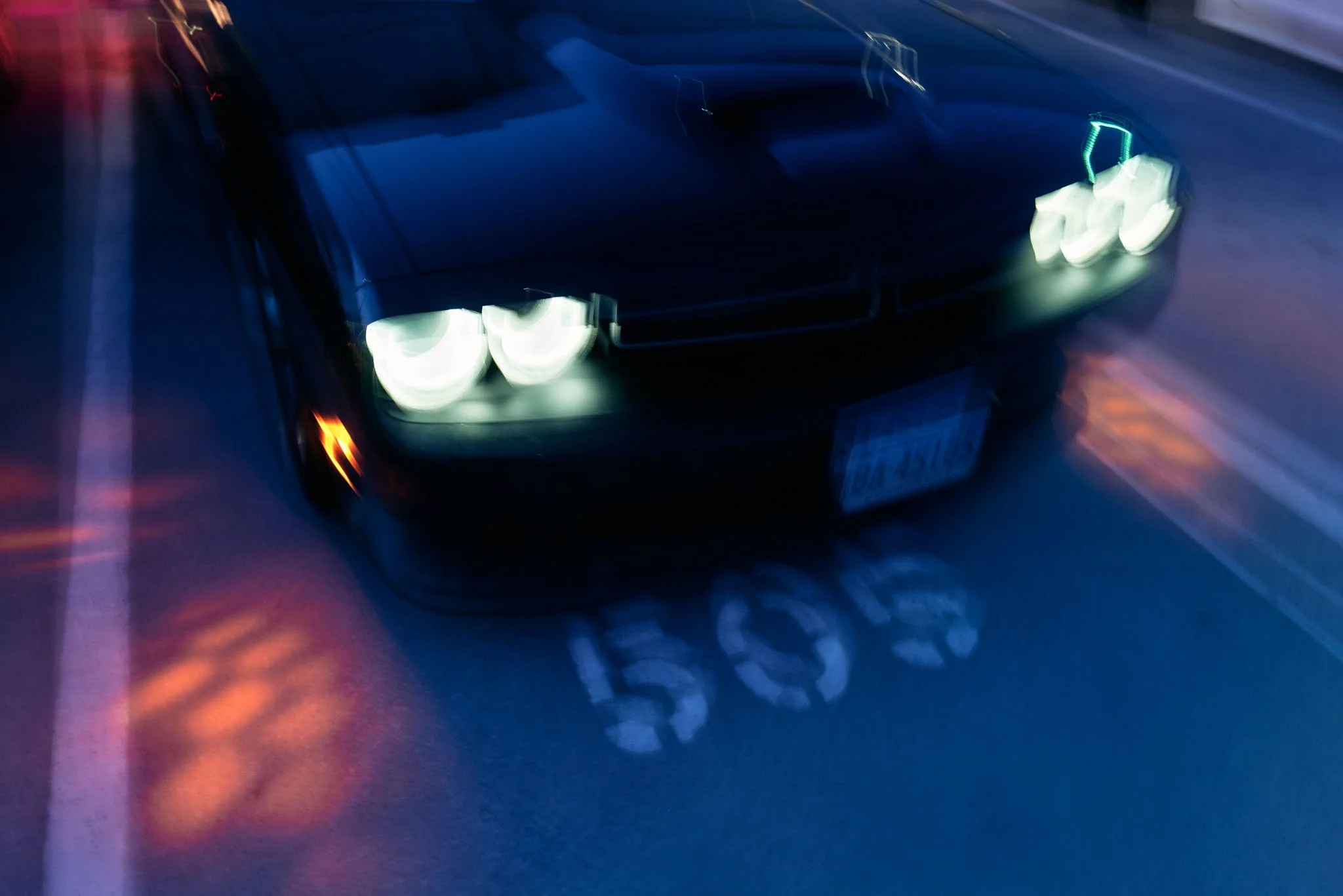 A black sports car with bright headlights driving on a road at night, with light trails and blurred surroundings.