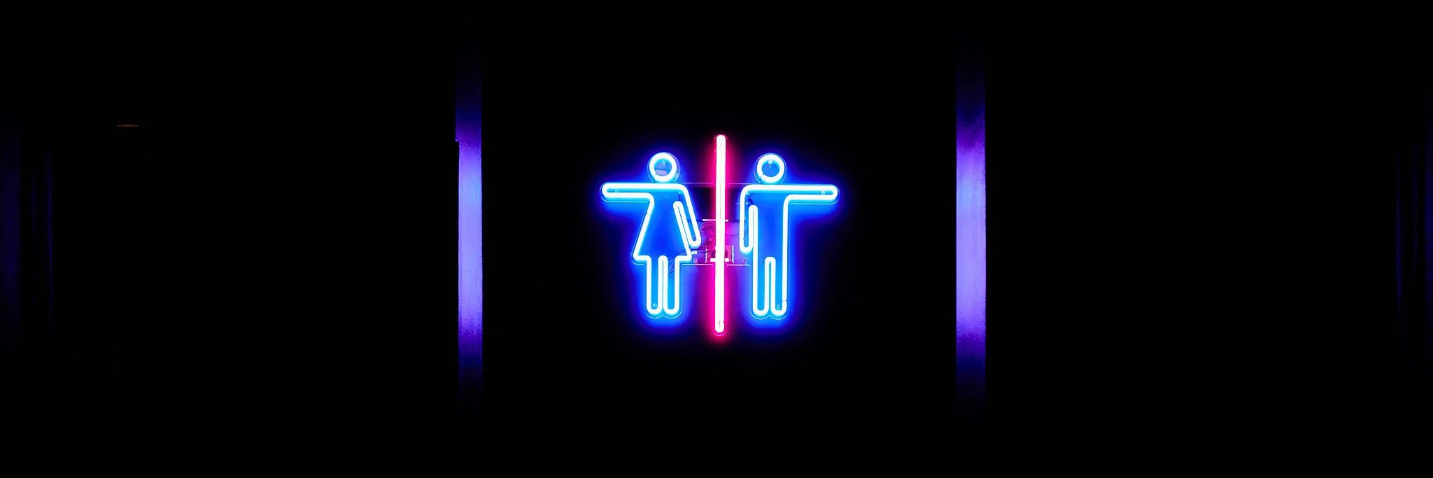 Neon sign of a woman and a man with a vertical line between them, indicating gender separation, against a dark background.