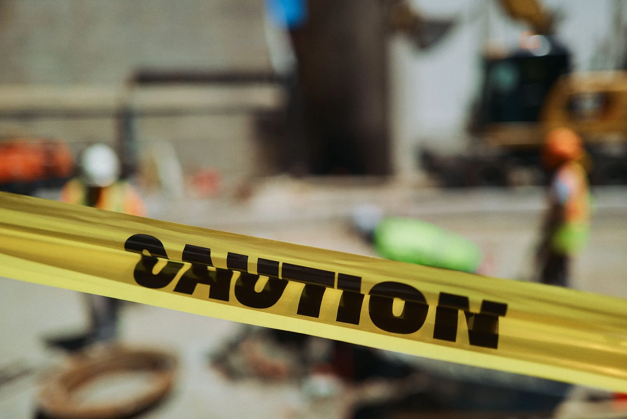 Construction site with caution tape in foreground and workers in safety gear in the background.