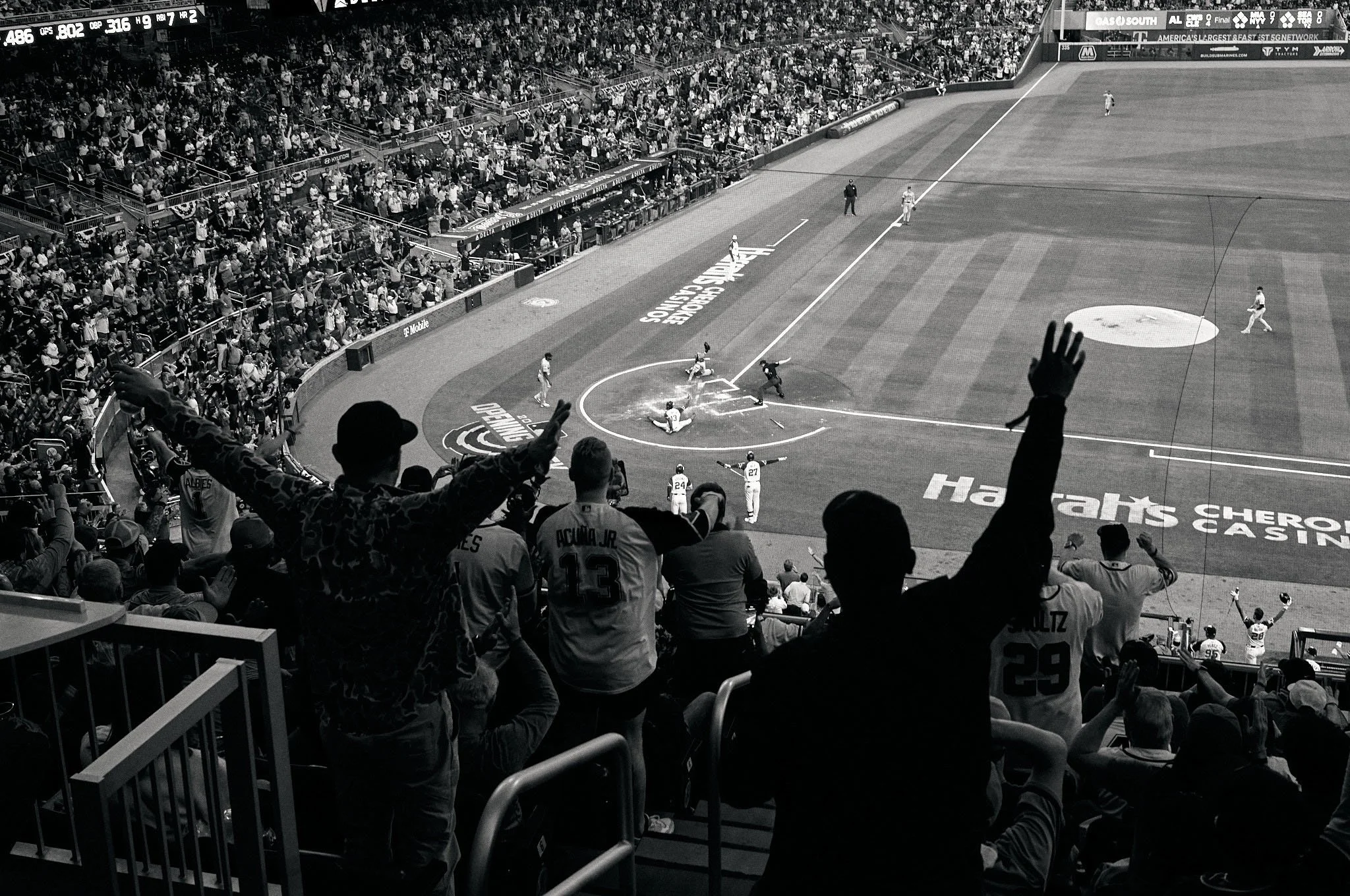Black and white photo of a baseball game showing players on the field and fans in the stands, some fans with their hands raised.
