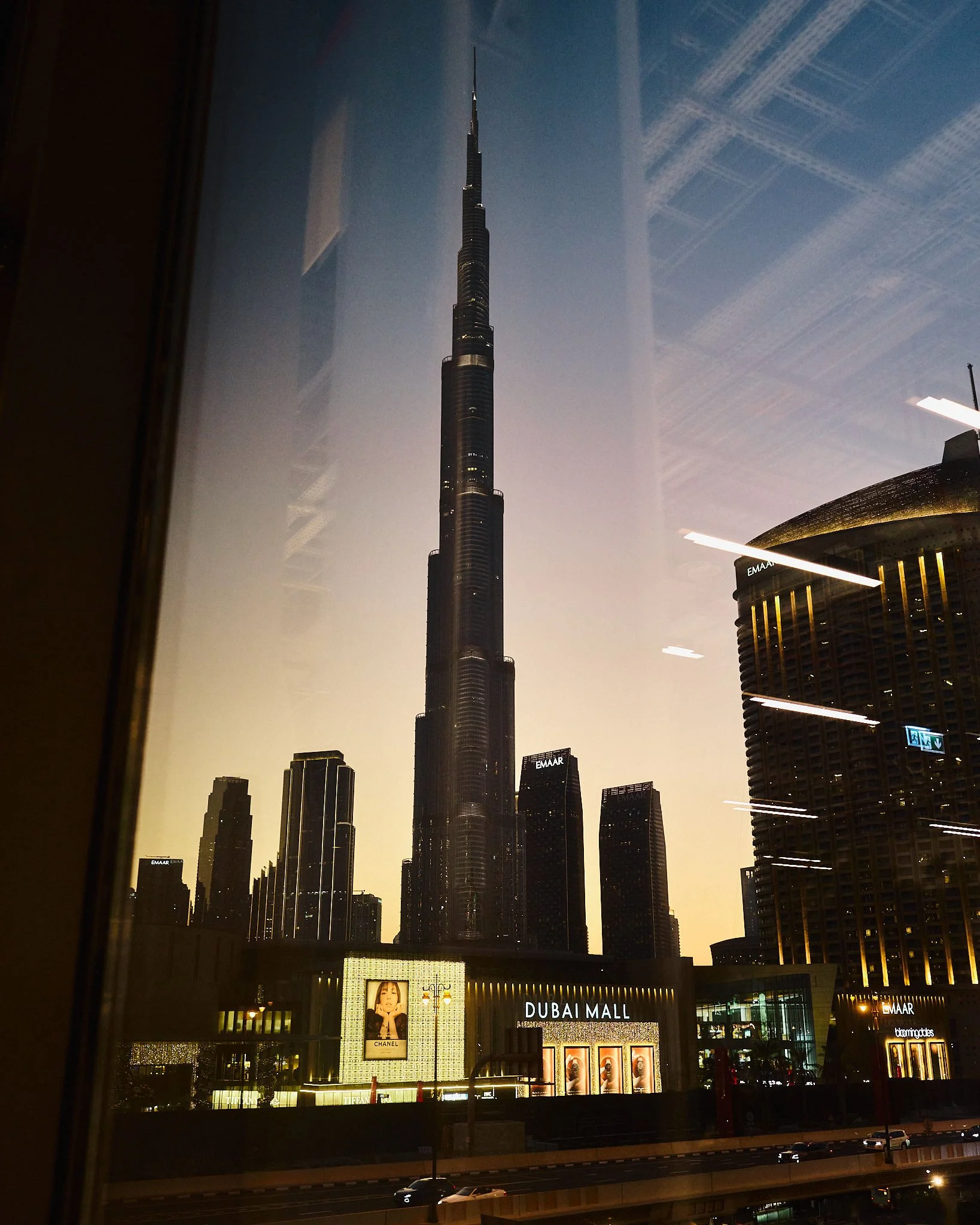 View of the Burj Khalifa skyscraper in Dubai at sunset, with Dubai Mall and several other tall buildings around it.