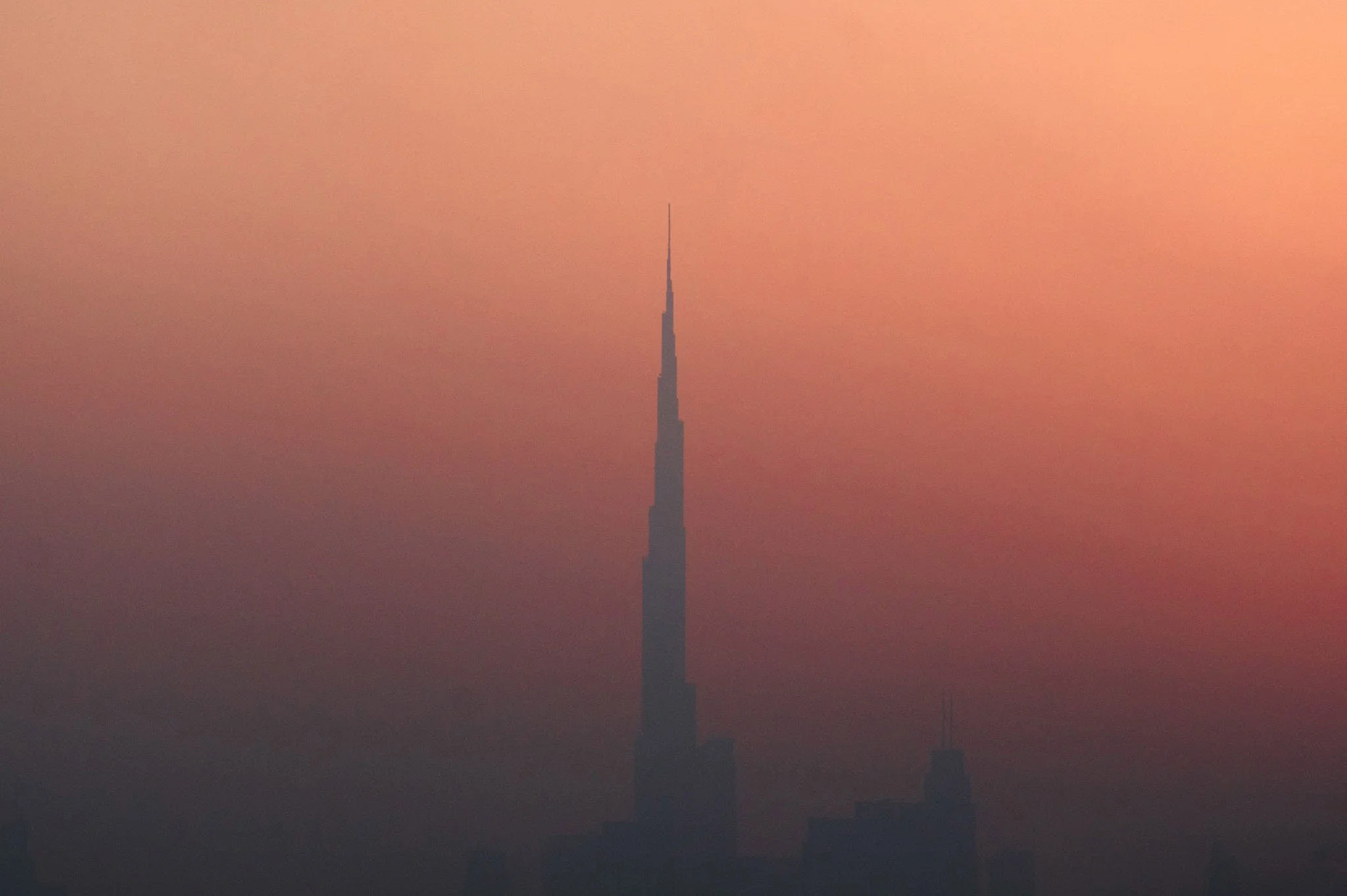 The image shows a silhouette of the Burj Khalifa against a pinkish-orange sky at dusk or dawn.