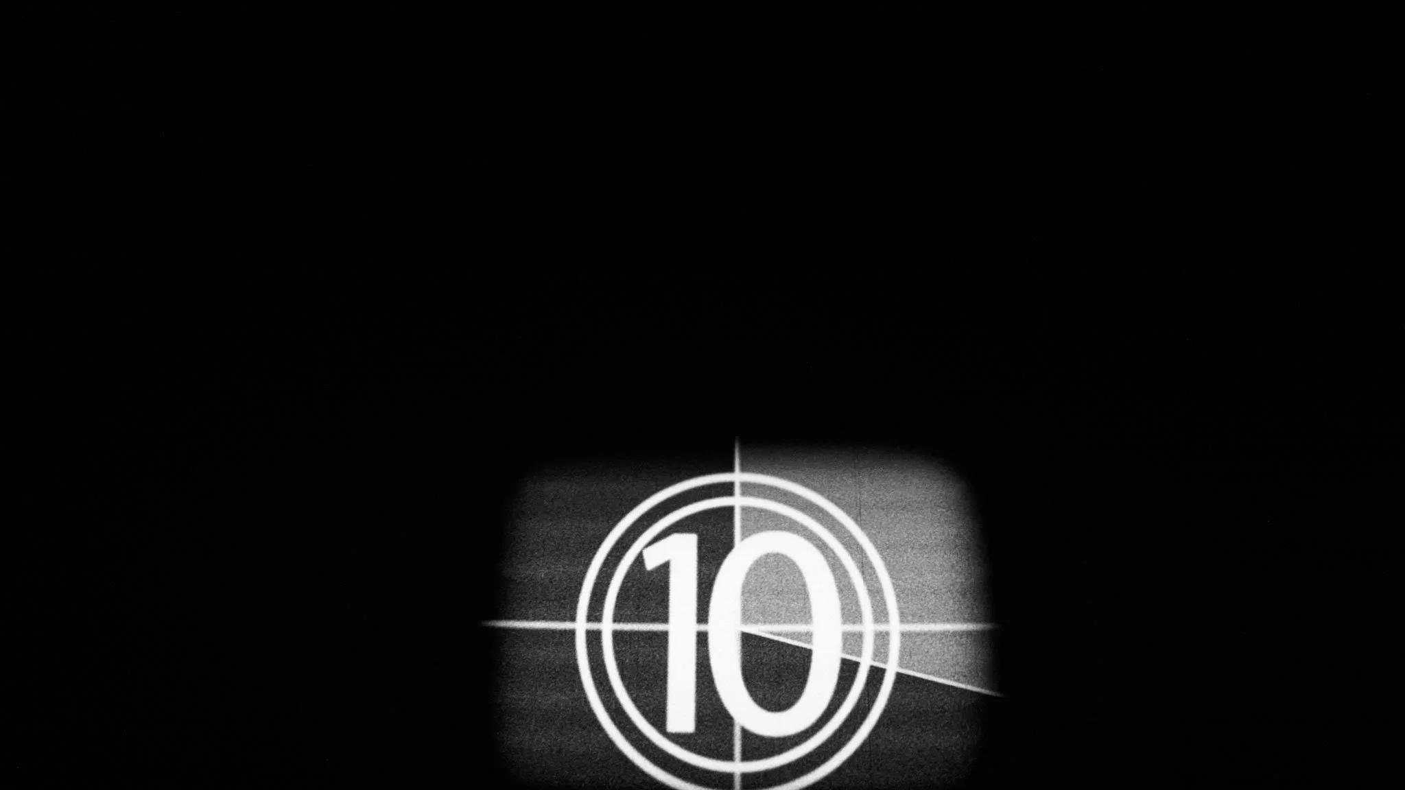 A black and white film countdown timer displaying the number 10, with concentric circles and crosshairs, projected on a dark background.