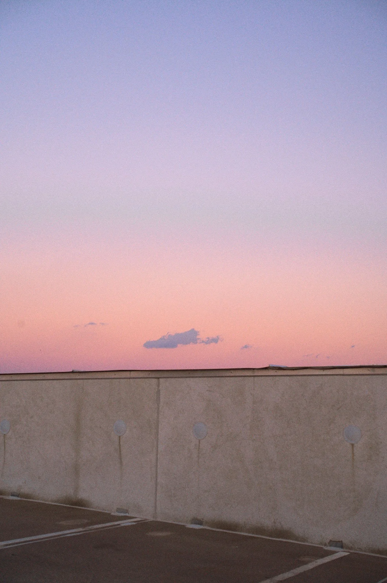Sky with pink and purple hues during sunset or sunrise over a concrete rooftop parking lot with a low wall.