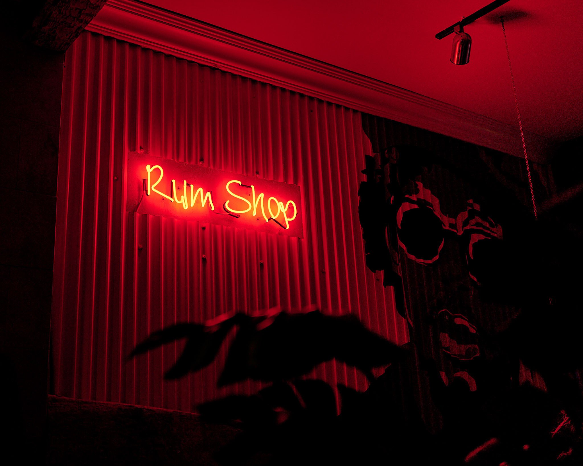 Red neon sign reading 'Rum Shop' on a striped wall inside a dimly lit room.