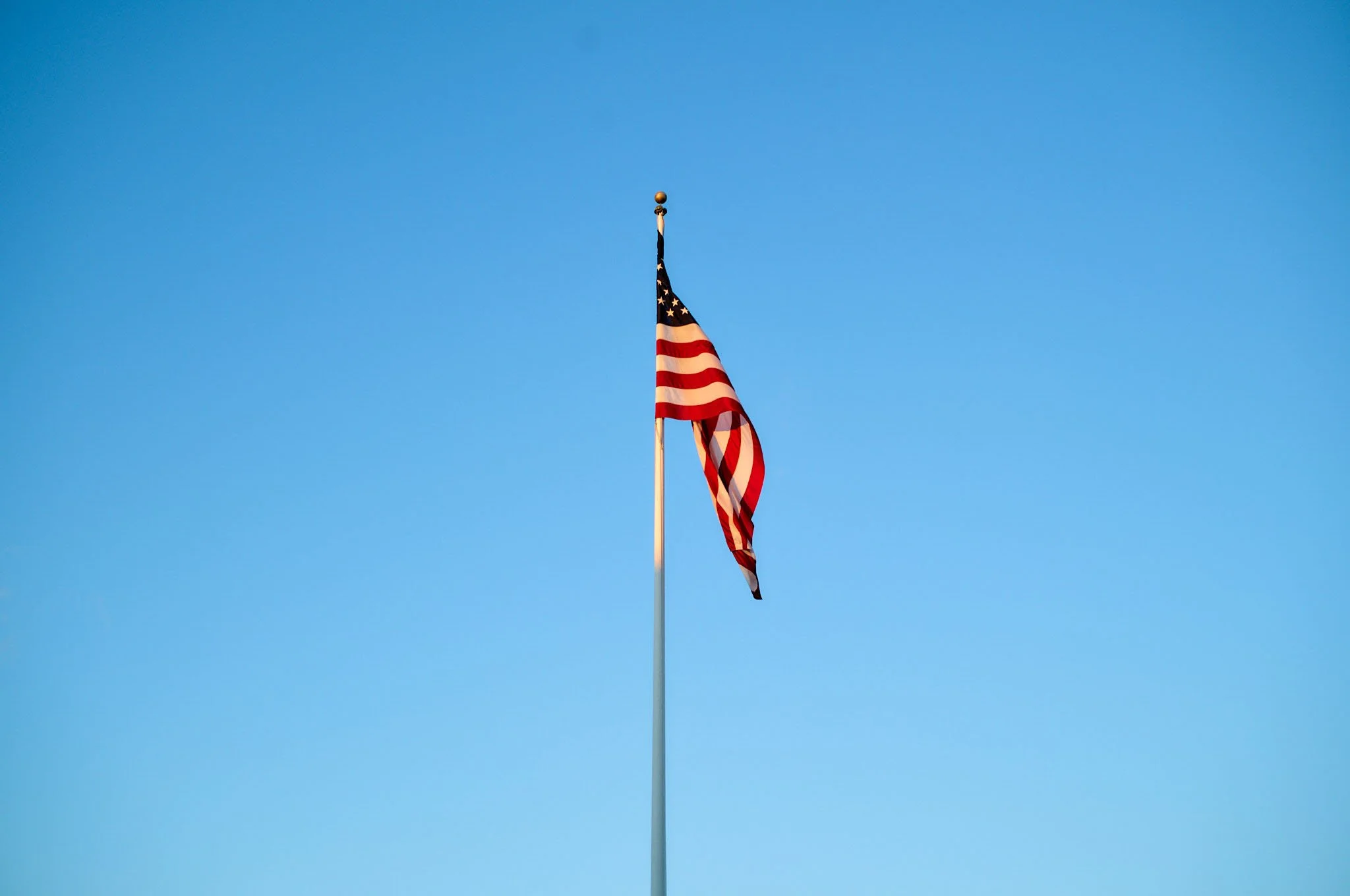 An American flag flying on a flagpole against a clear blue sky.