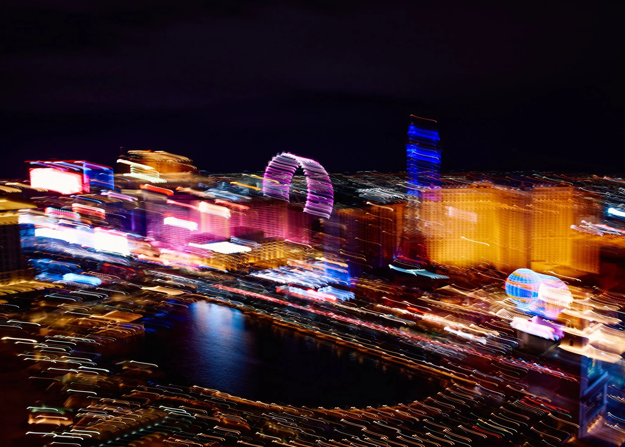 Blurred night view of a city skyline with colorful lights and reflections on the water.