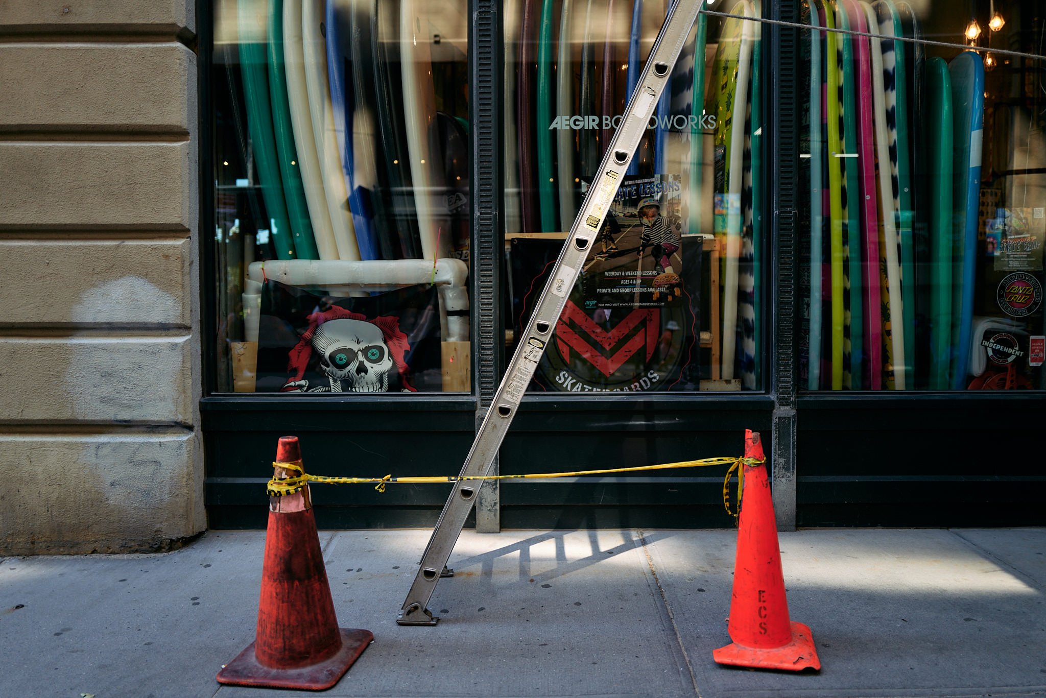 Construction cones and a ladder outside a storefront window with colorful skateboards and skateboarding posters