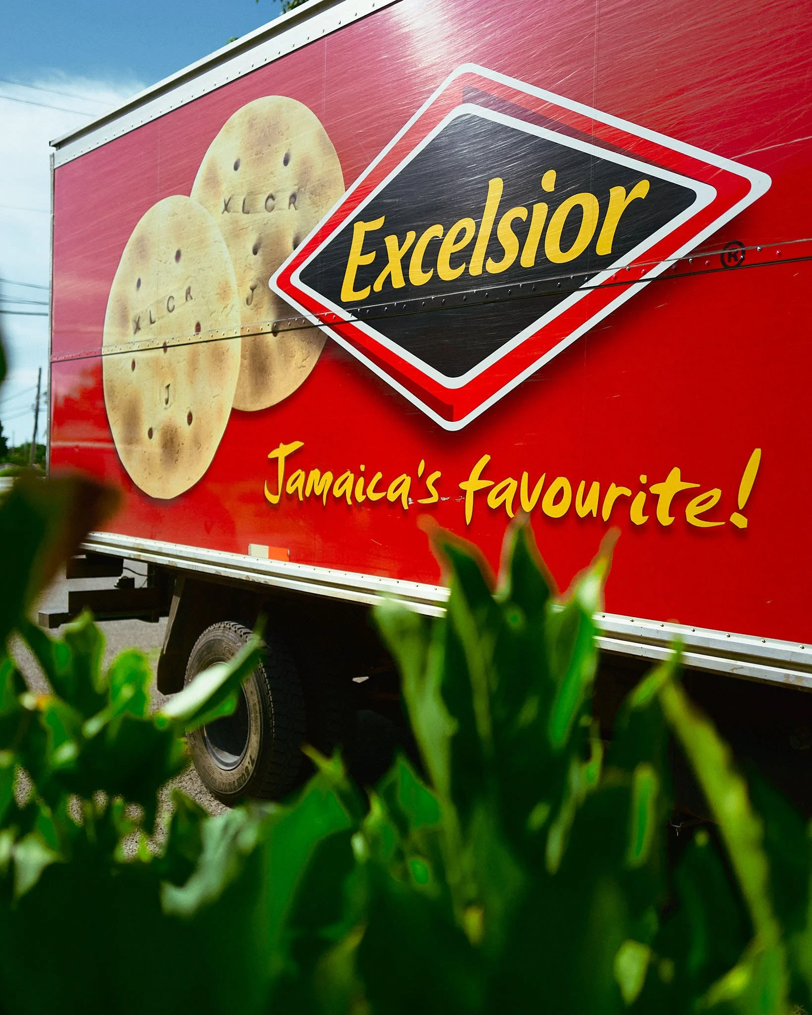 A bright red billboard advertising Excelsior crackers with an image of two crackers and the tagline 'Jamaica's favourite!'