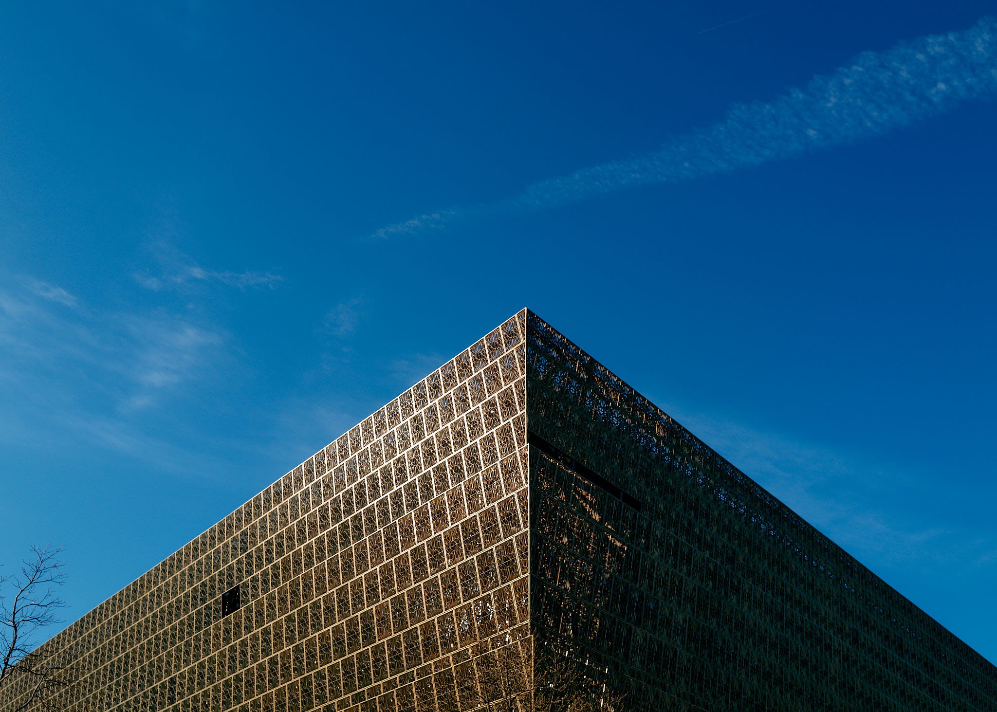 Close-up of a geometric modern building with a triangular corner, covered in reflective glass panels, against a bright blue sky.