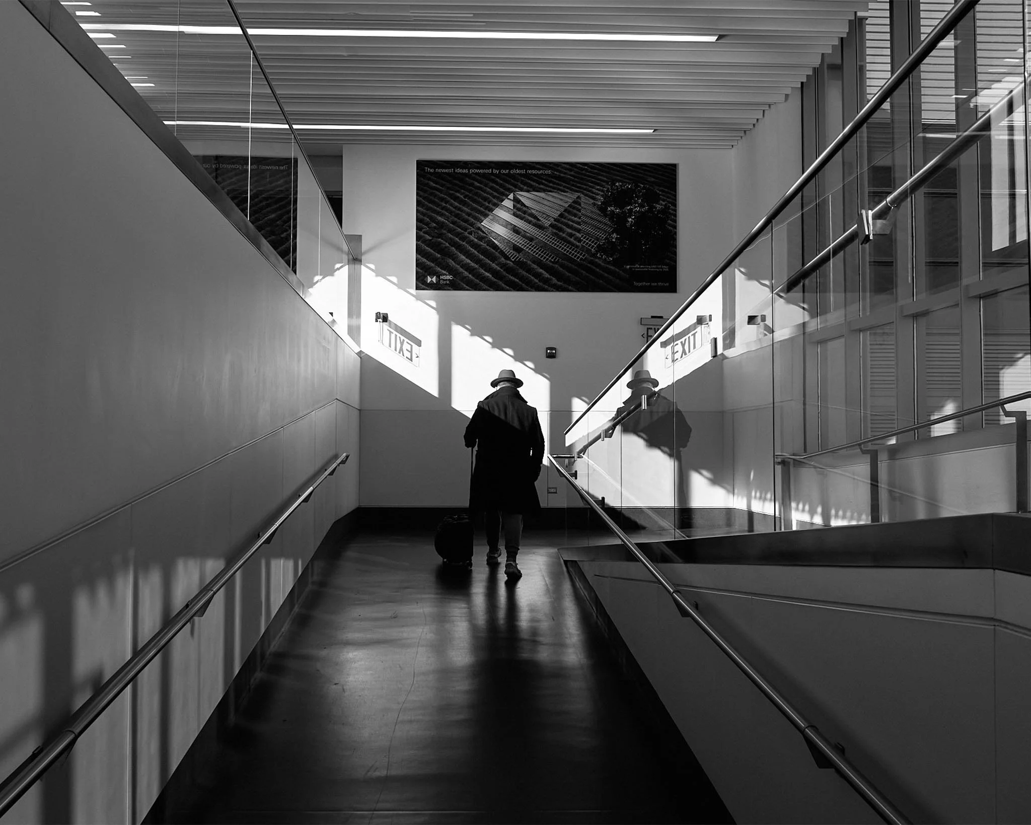 A person walking in an airport or train station with a suitcase, in black and white.