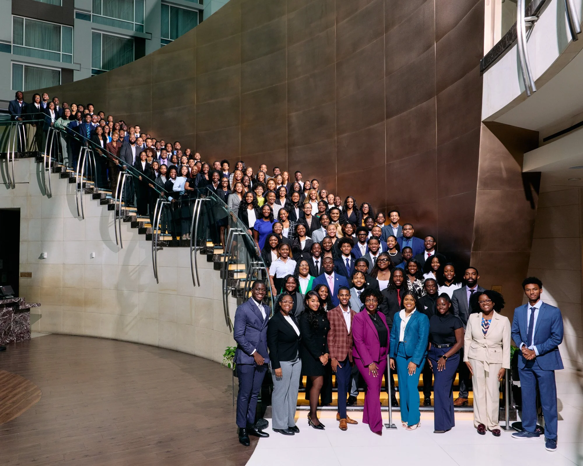 A large group of people dressed in business attire, gathered on a staircase in a modern building for a formal photo.