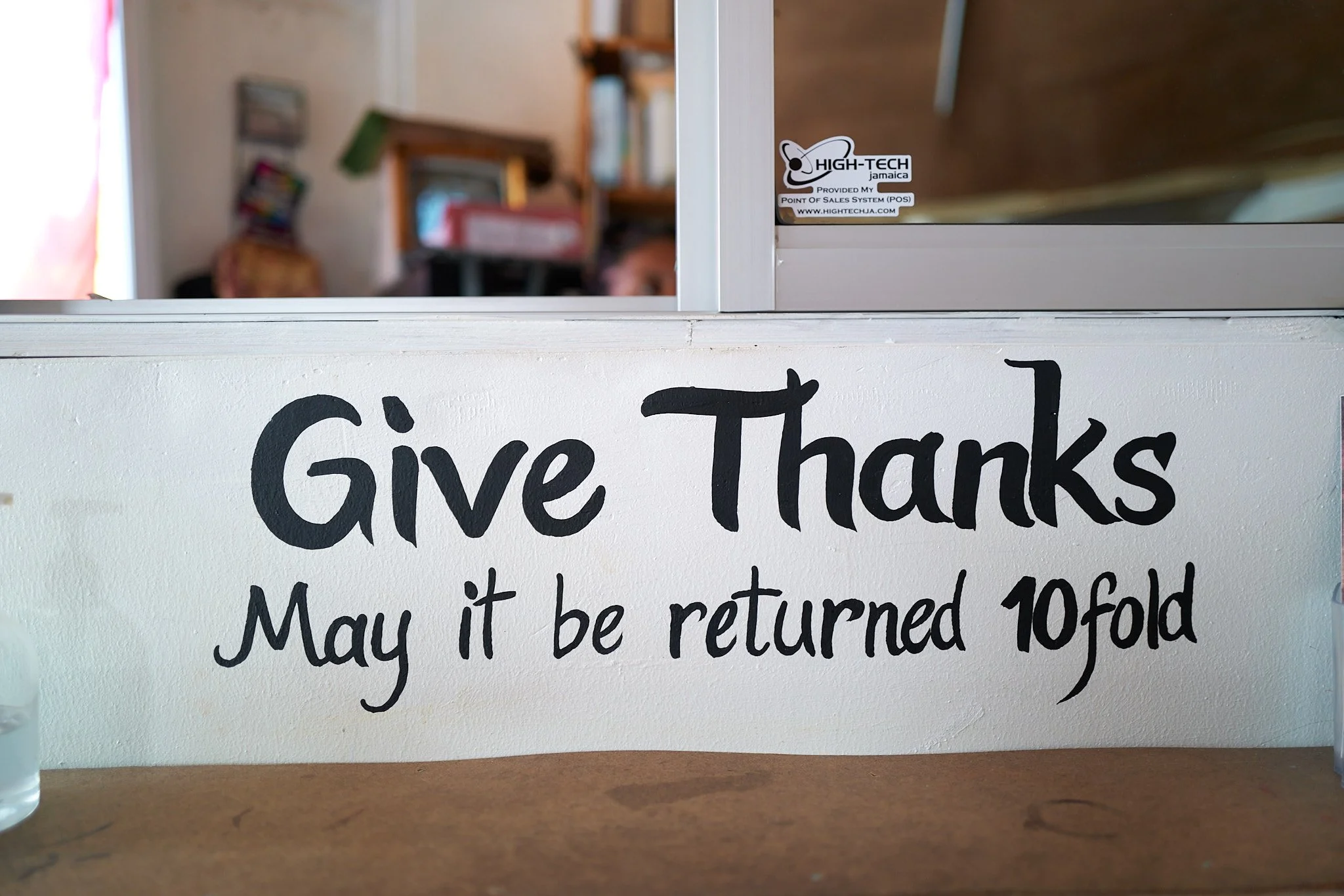 White sign with black handwritten text reading, 'Give Thanks. May it be returned 10 fold.'