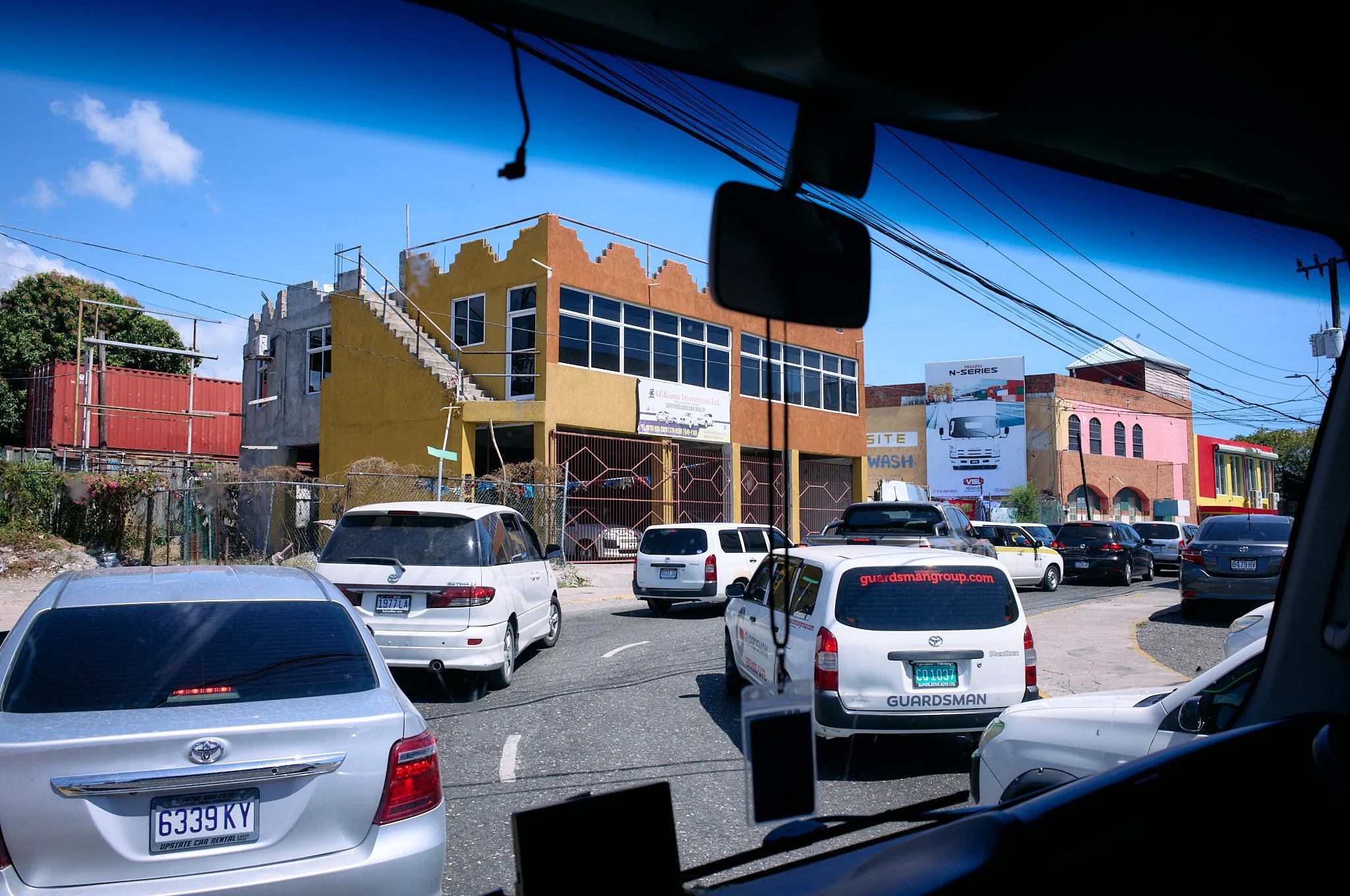 City street view from inside a vehicle showing parked cars and colorful buildings.