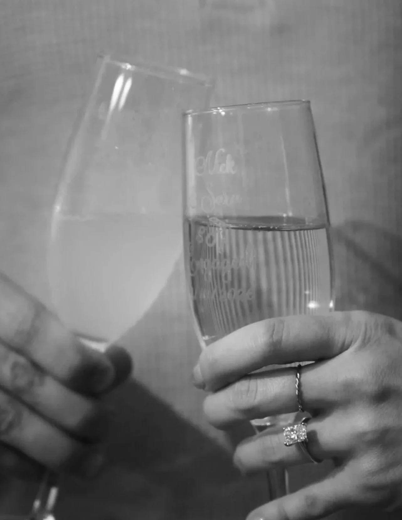 Two hands holding glasses, one filled with water and the other partially filled, clinking together in a toast.