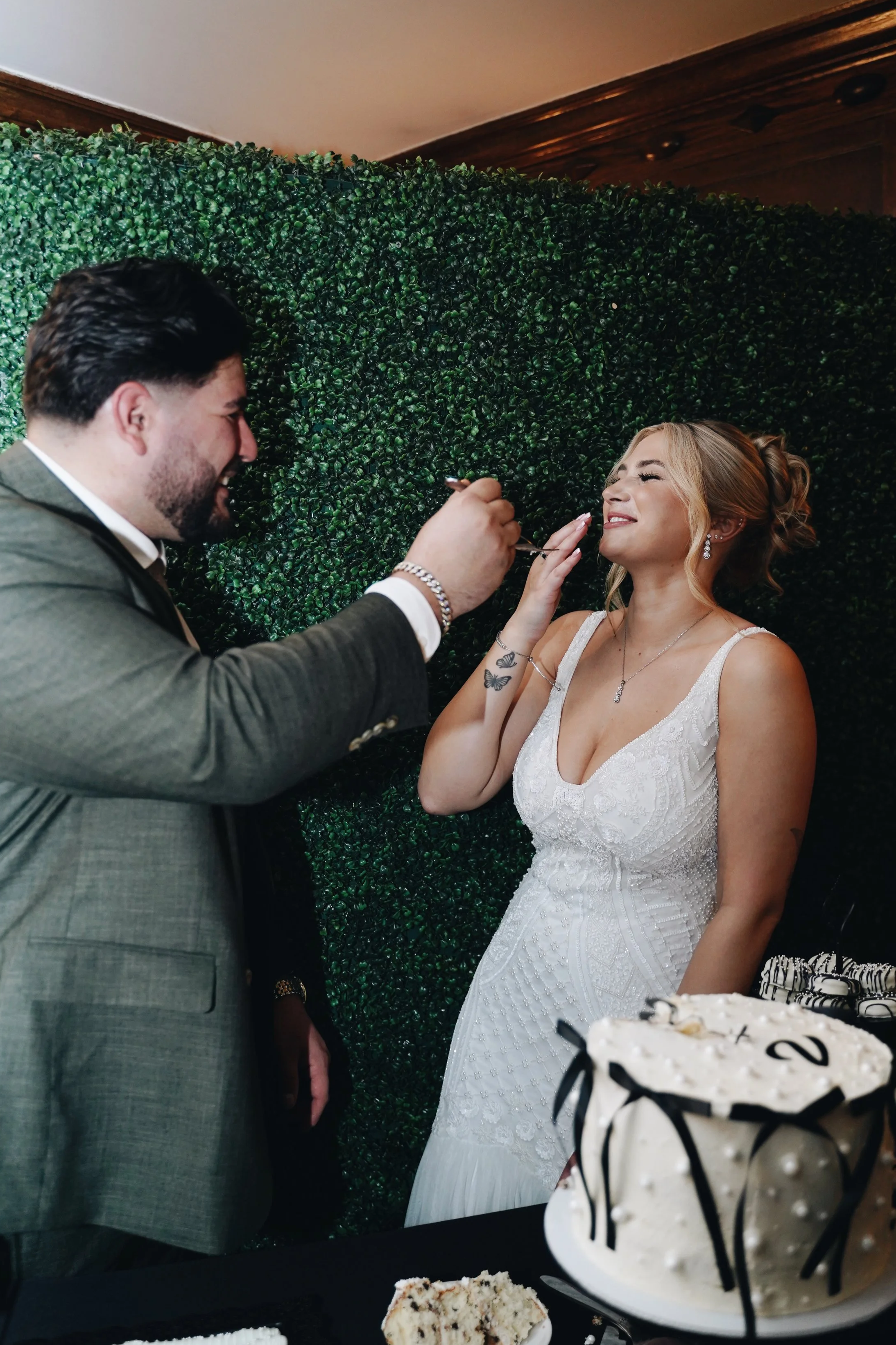 A man feeding a woman cake at a celebration, with a green leafy backdrop and a cake in the foreground.