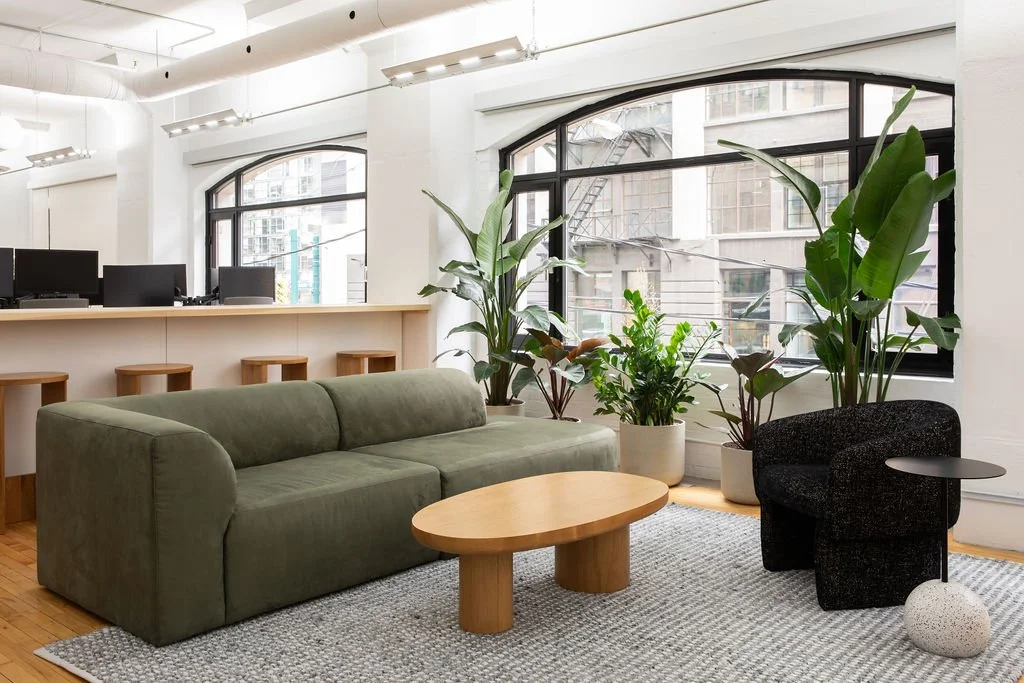 Contemporary office lounge at HelloFresh in Toronto, designed by Flodström Interiors with a sage green sofa, sculptural oak coffee table, black lounge chair and natural light from industrial windows.