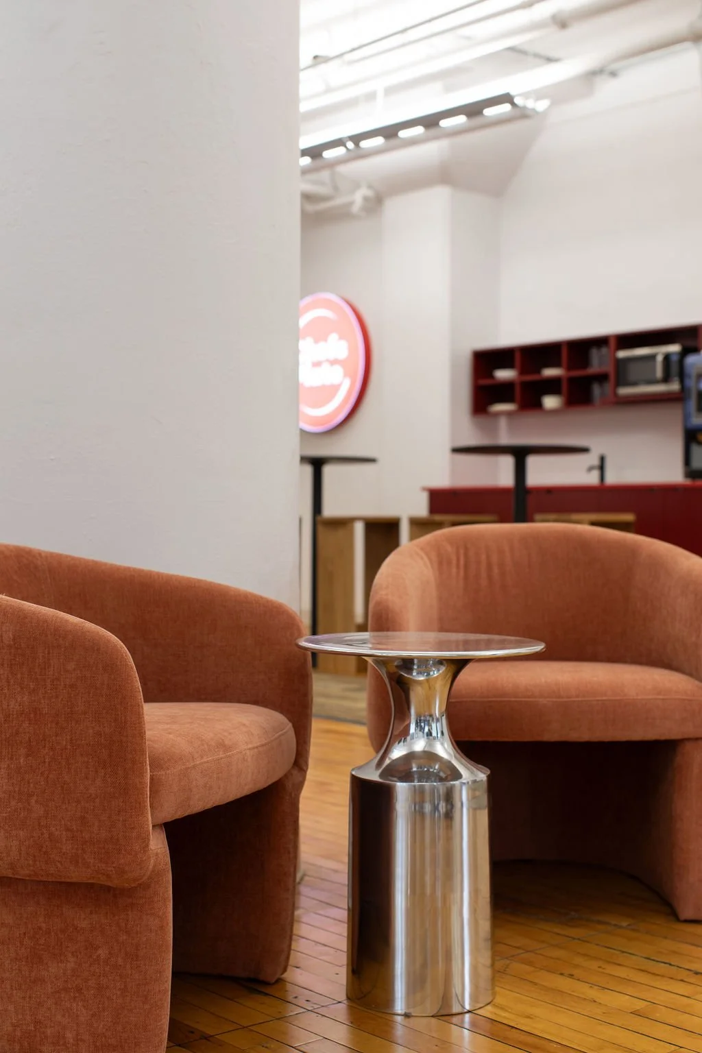 Informal lounge seating at the Chef's Plate Toronto office, designed by Flodström Interiors with rust-coloured upholstered chairs, a sculptural silver side table and warm wood flooring.
