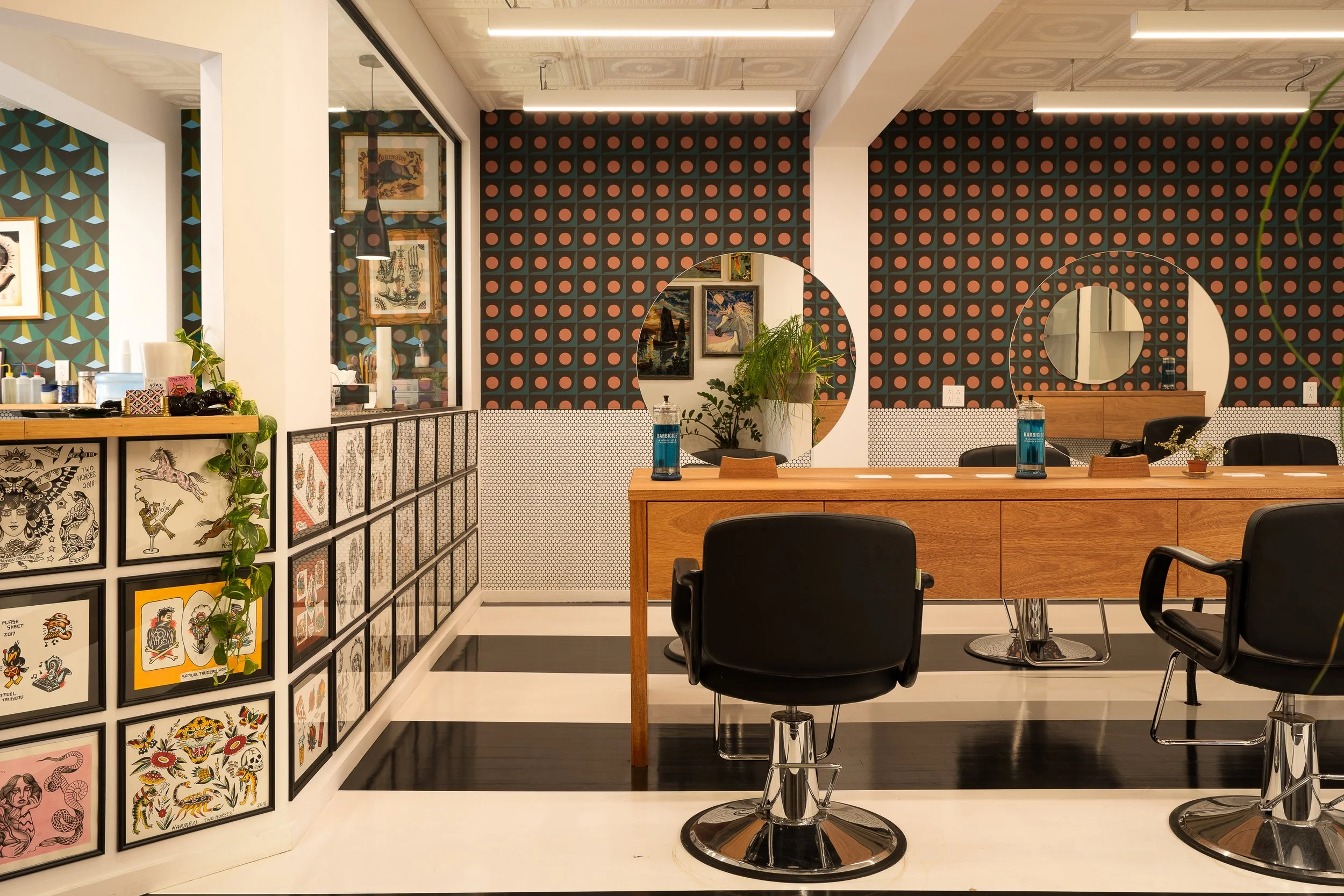 Interior view of Two Horses showing the custom salon styling stations, black-and-white striped floors and glass-partitioned tattoo studio.