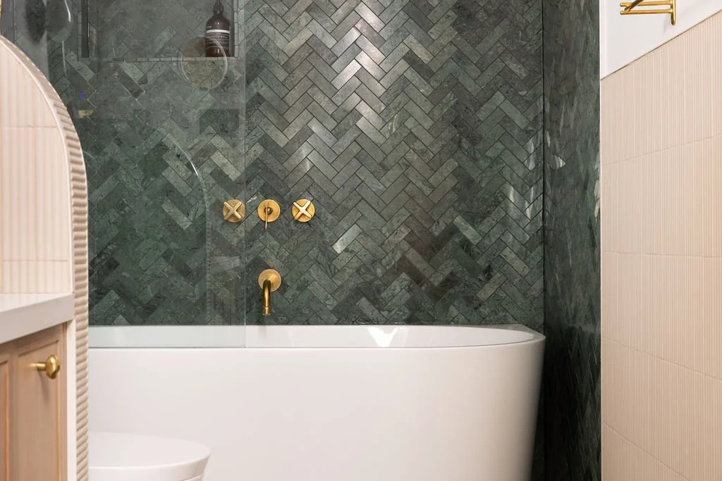 Toronto bathroom renovation featuring a freestanding white bathtub, deep green herringbone stone tile and wall-mounted brass fixtures.