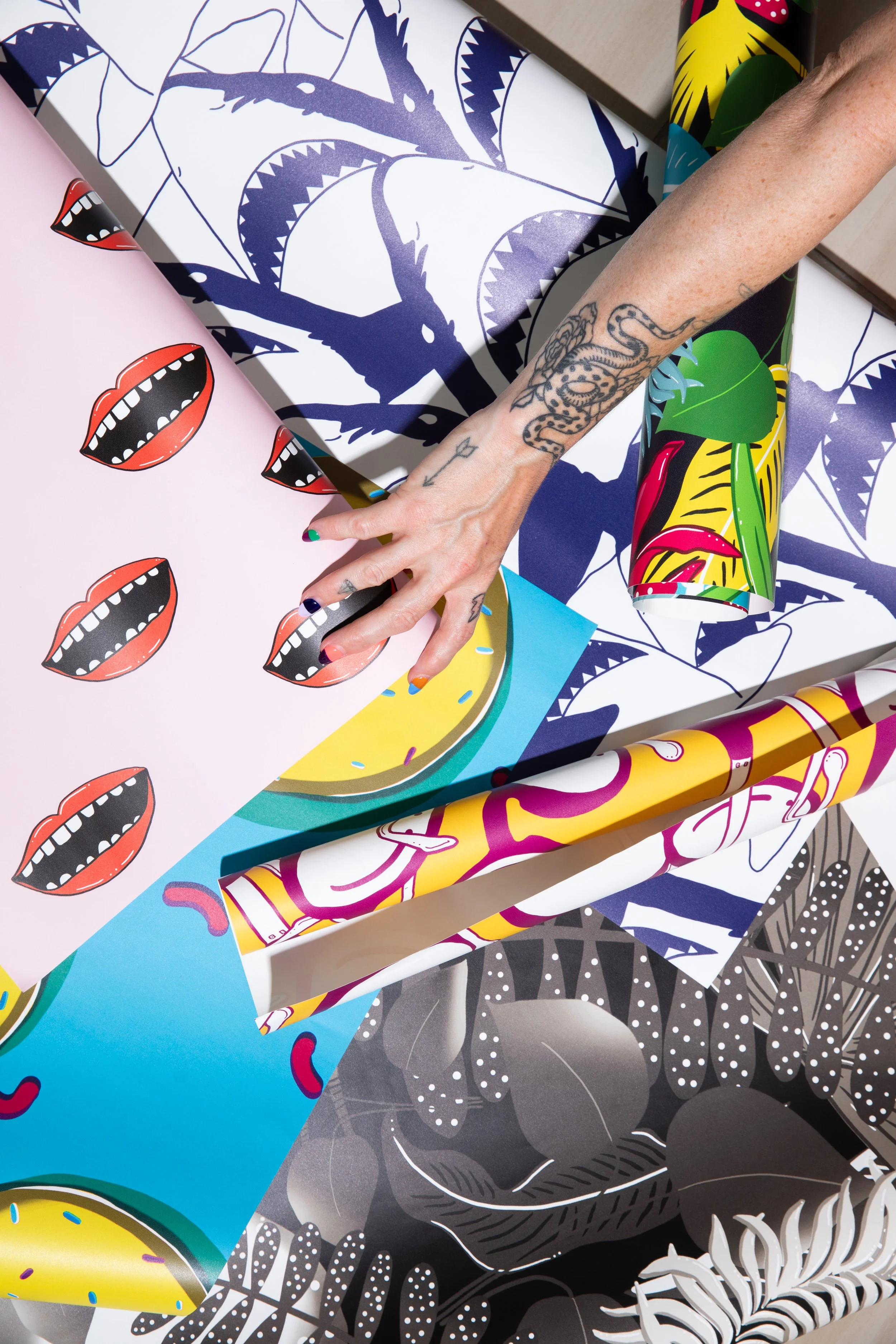 Overhead photograph of illustrated wallpaper rolls featuring sharks, colourful tropical patterns and graphic mouths.