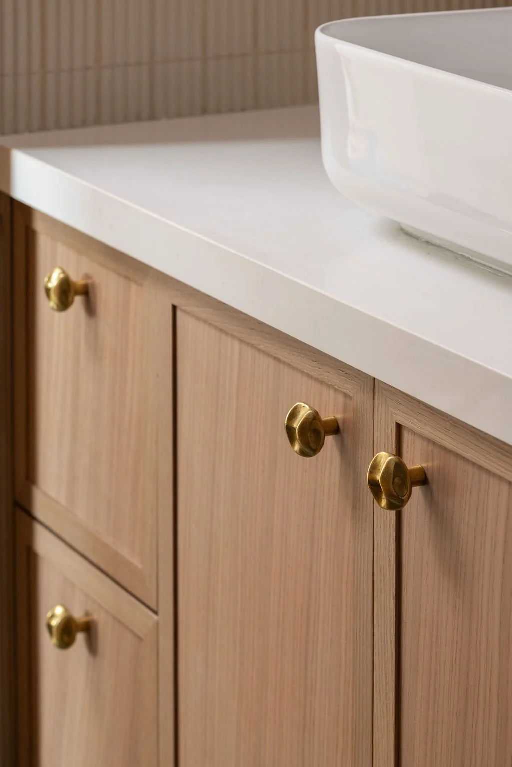 Close-up of natural oak bathroom cabinetry with brass knobs and a white countertop.